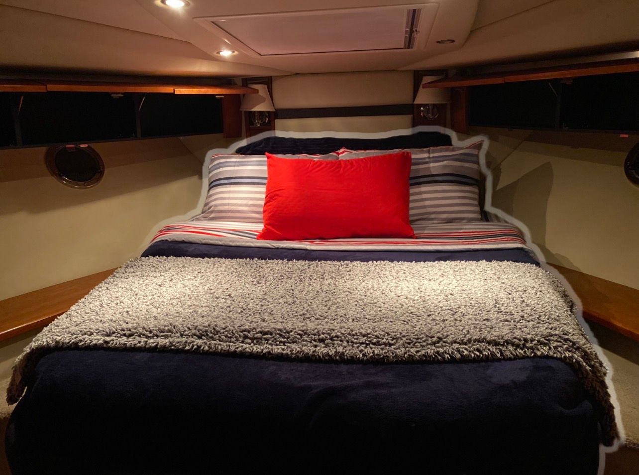 The image shows a cozy cabin with a double bed, decorated with striped bedding and a red pillow.