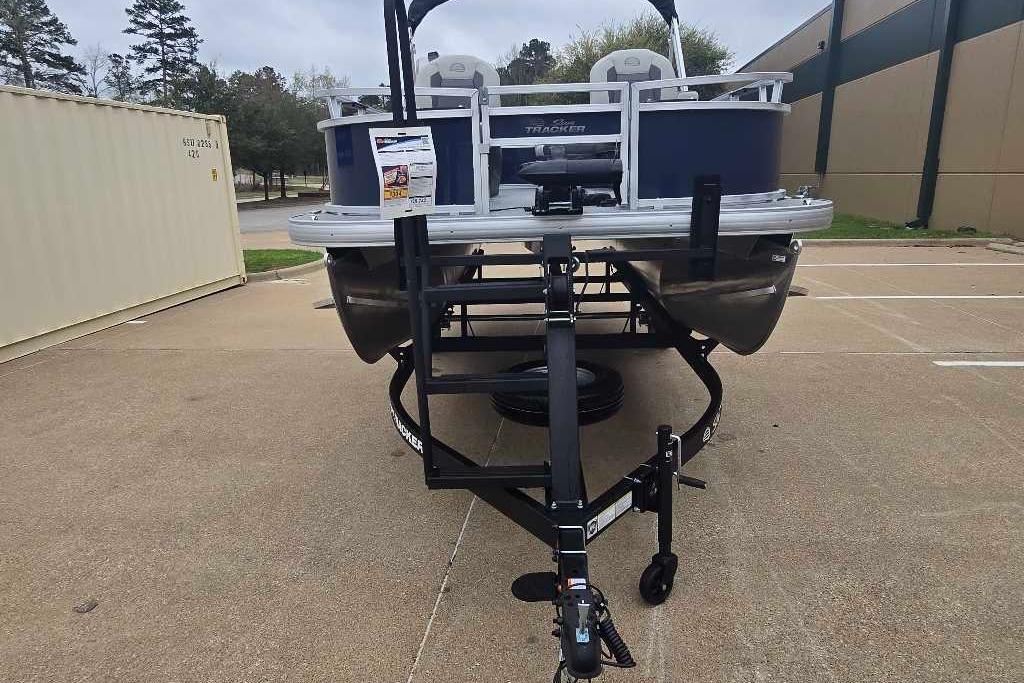 2026 Sun Tracker Bass Buggy 16 XL Select pontoon boat on trailer in parking lot.
