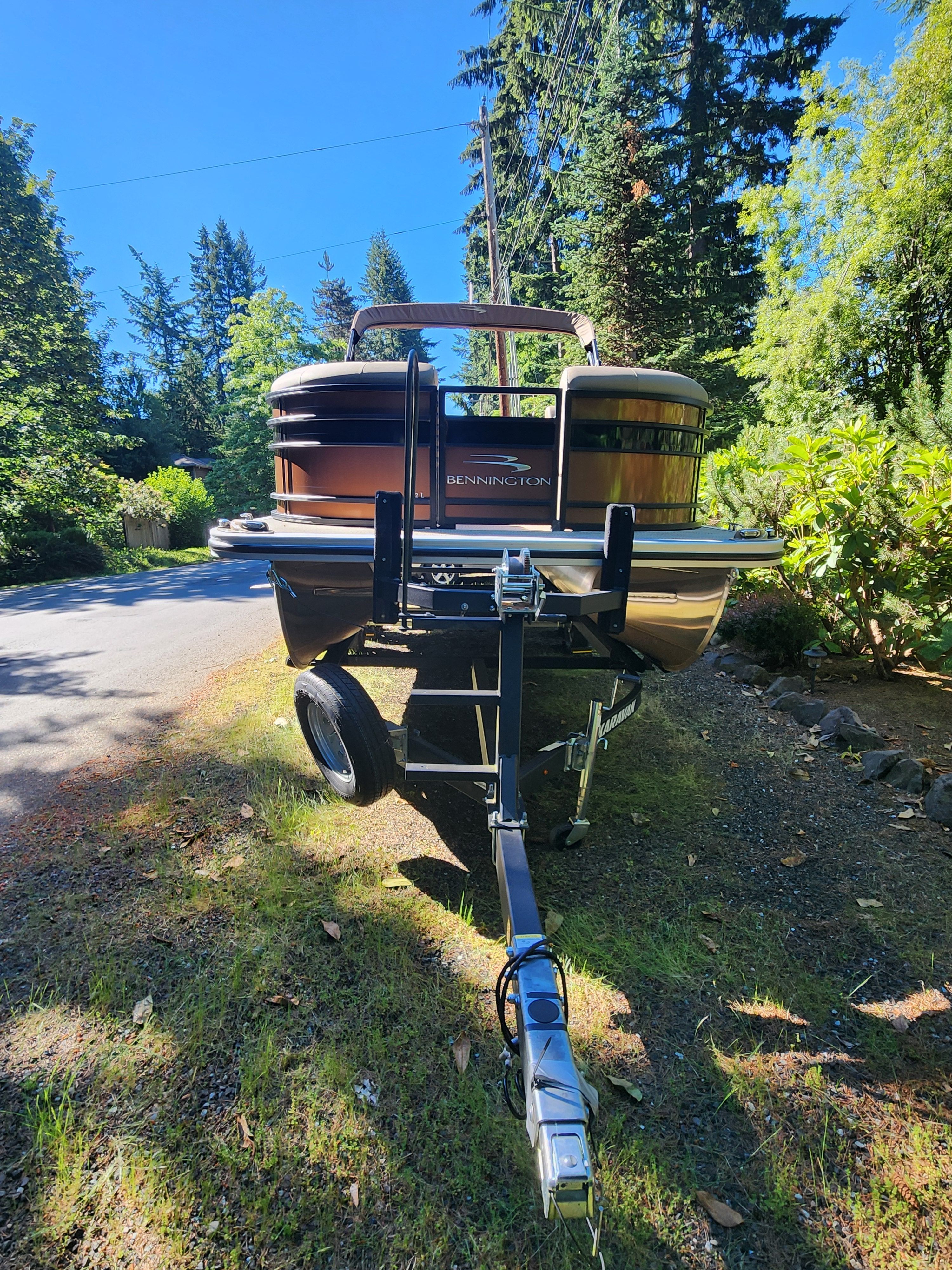 A Bennington 22 LSB pontoon boat on a trailer in a wooded setting.