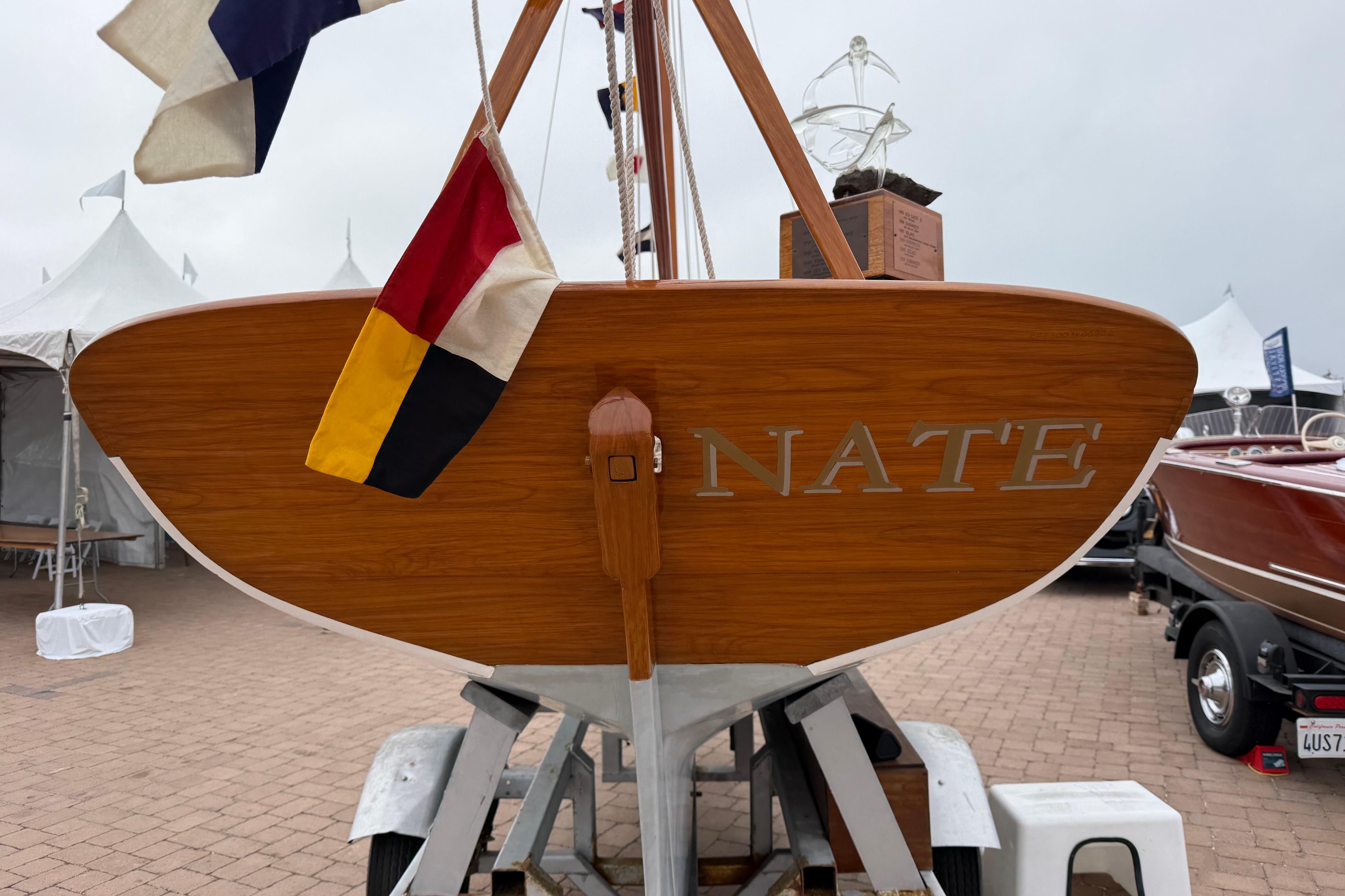 1920 Herreshoff 12.5 sailboat with flags, displayed on a trailer at a boat show.