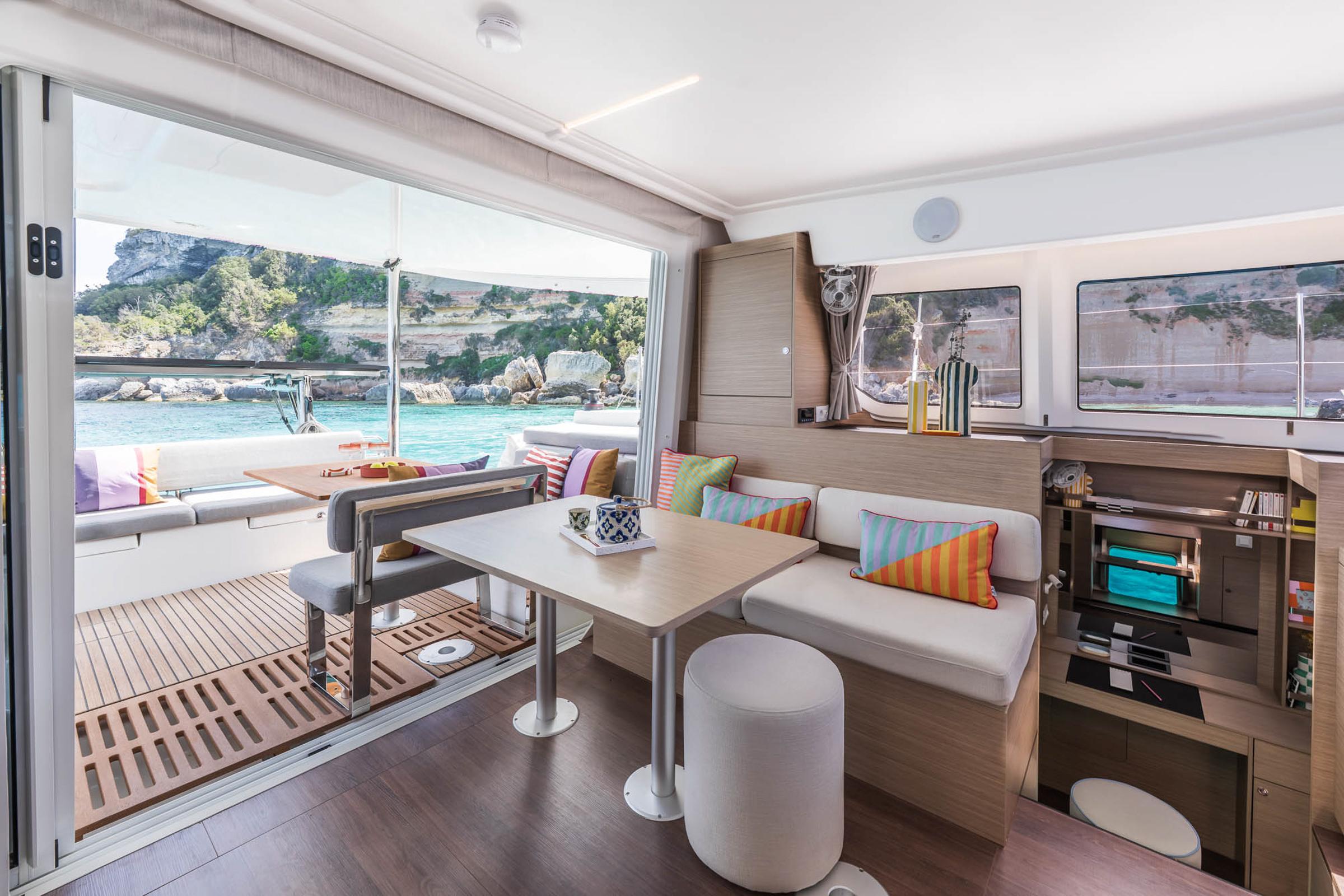 Modern interior of 2025 Lagoon 38 catamaran with colorful cushions and scenic ocean view.
