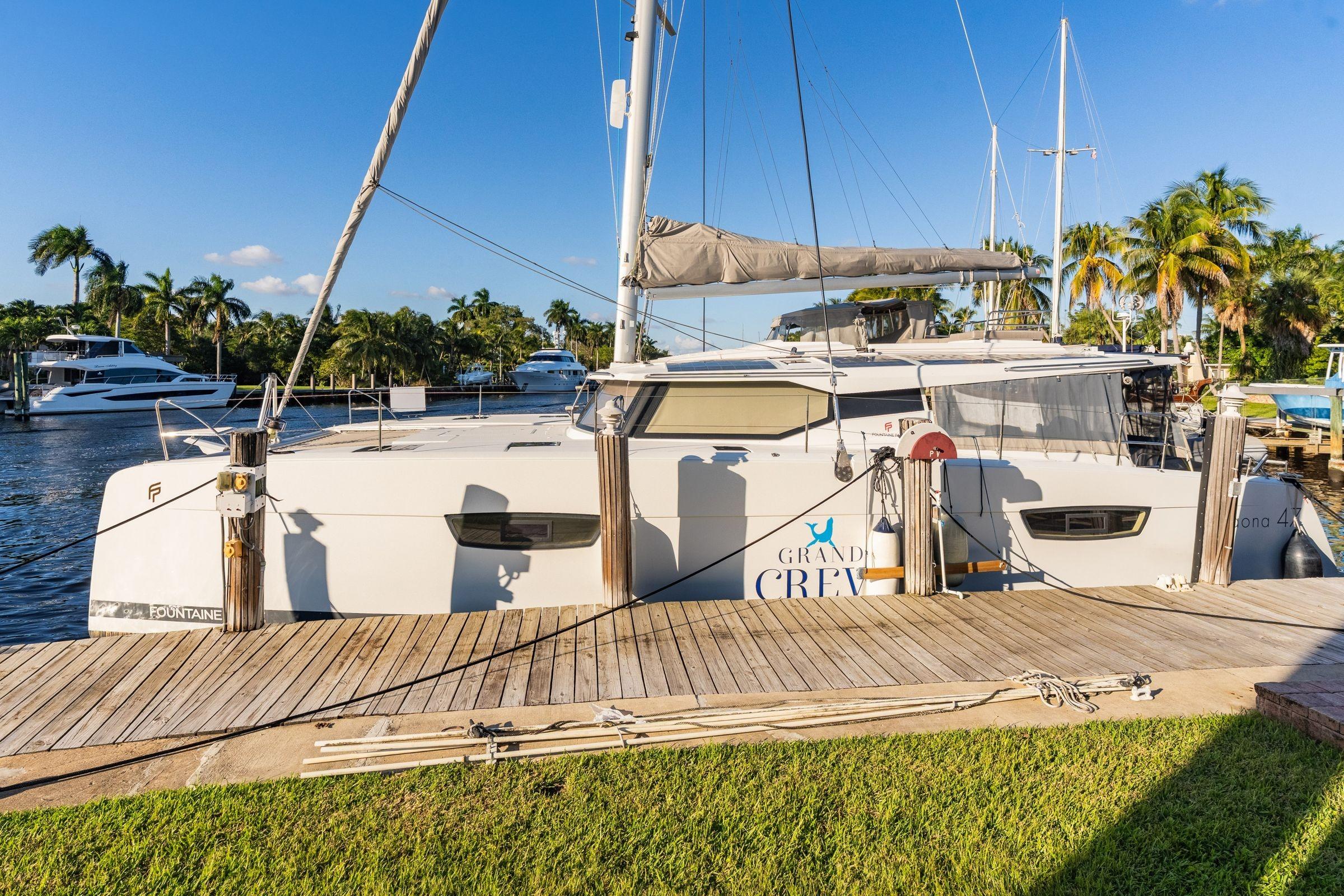 2019 Fountaine Pajot 47 catamaran docked, surrounded by palm trees and clear blue sky.