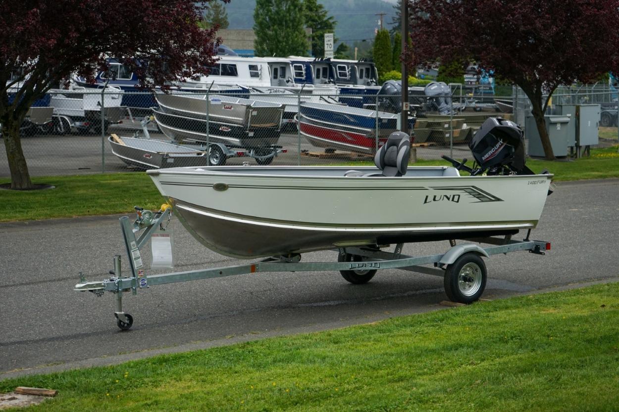 2026 Lund 1400 Fury Tiller boat on trailer, parked near marina with other boats.