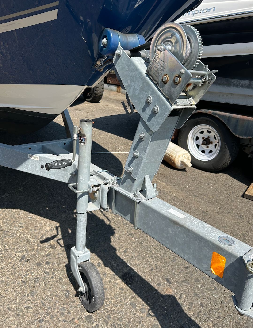 Close-up of a boat trailer with a winch and support wheel on a parking lot.