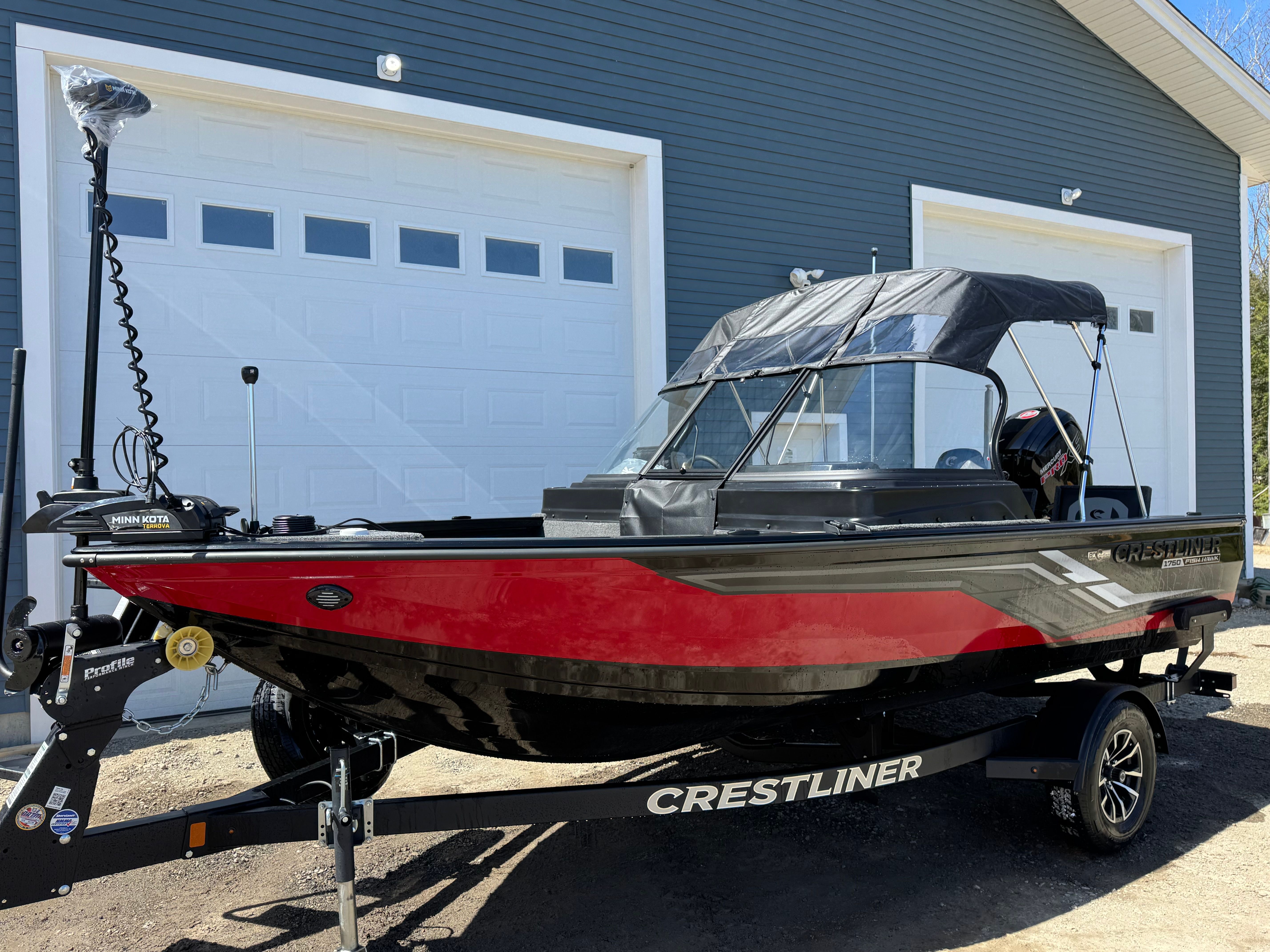 A red Crestliner boat is on a trailer in front of a garage.