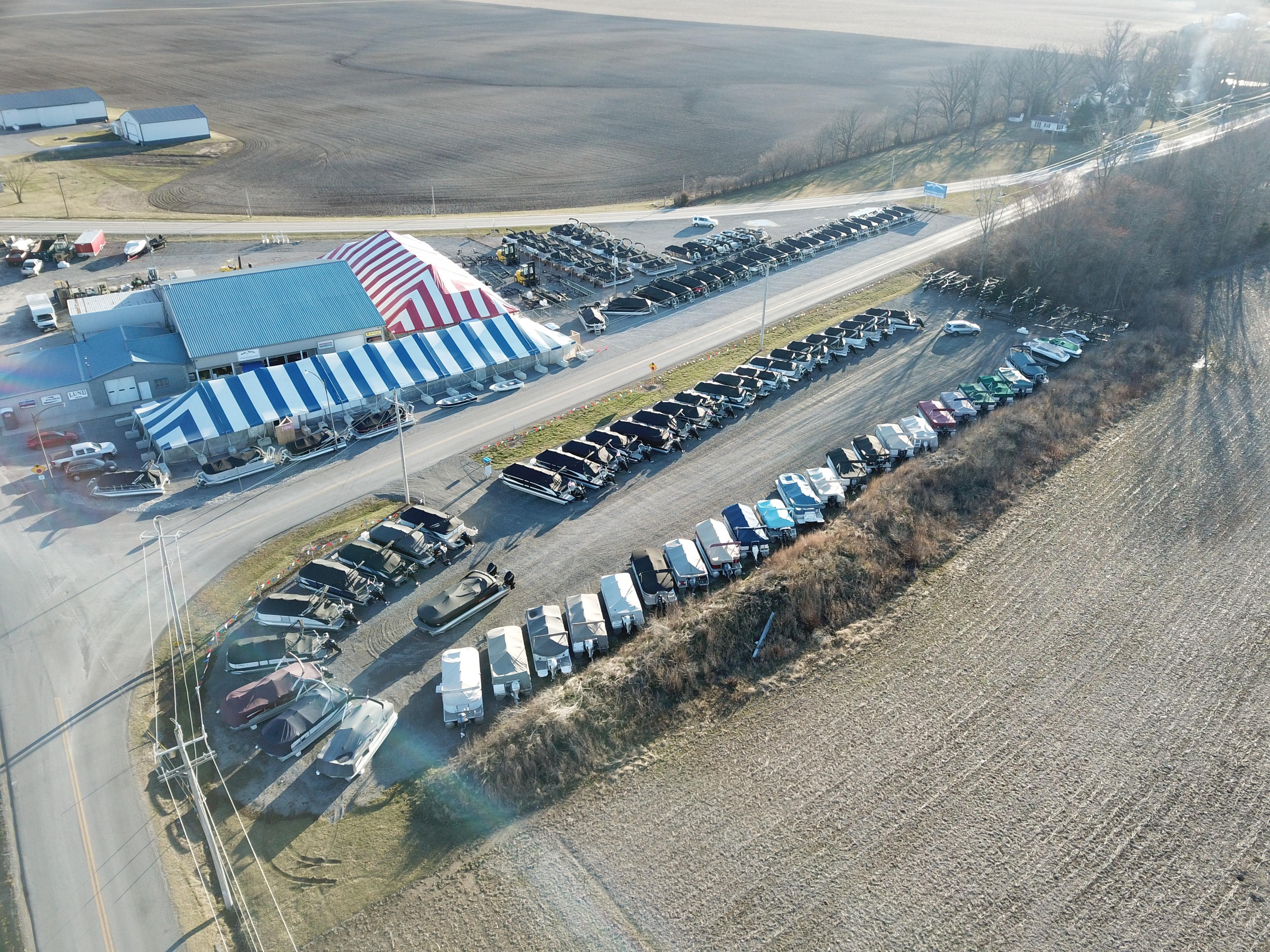Aerial view of a large parking lot with numerous vehicles near a striped tent.