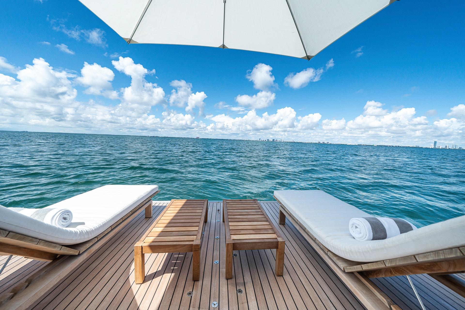 Luxurious Azimut Grande 27 METRI yacht deck with sun loungers, ocean view, and blue sky.