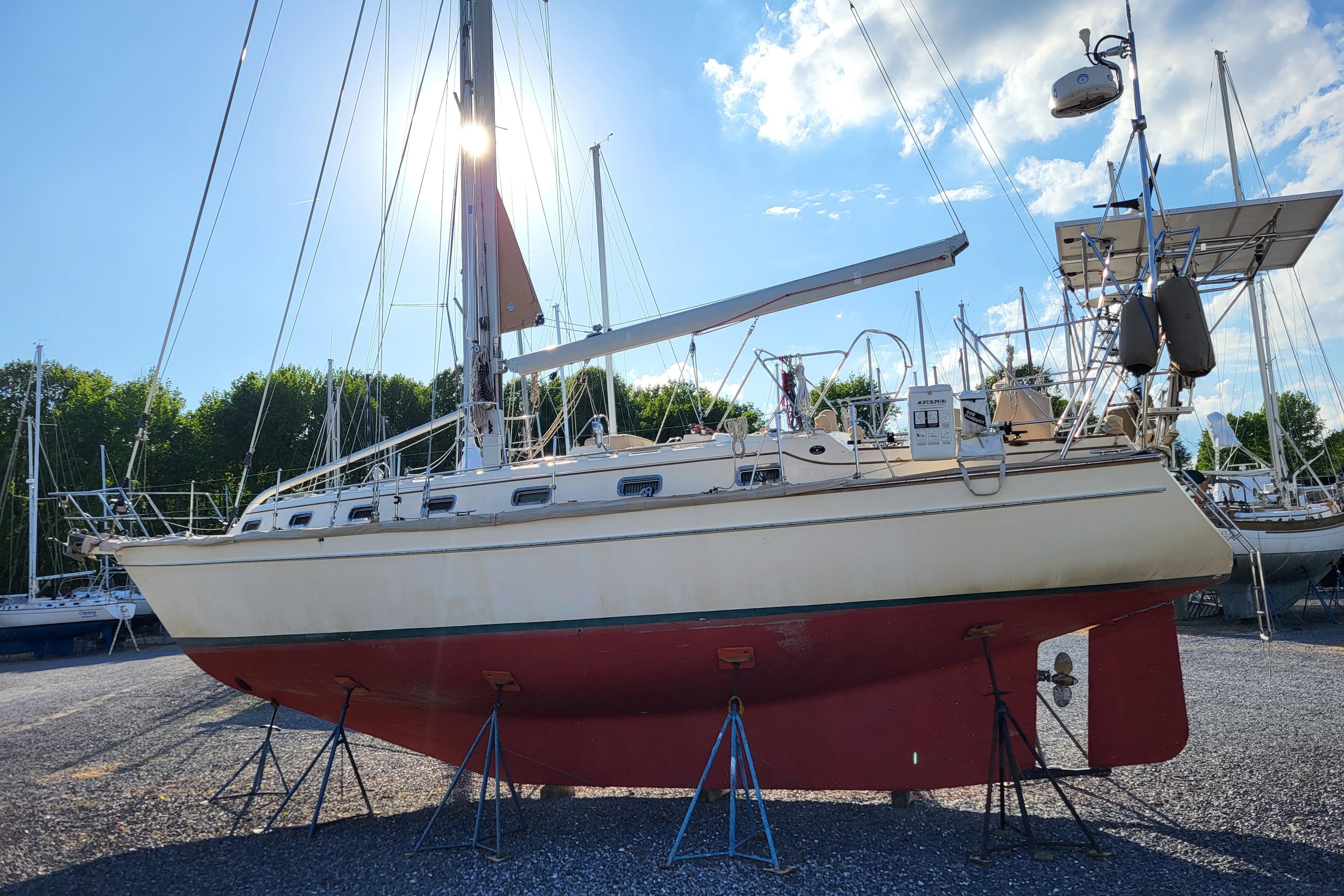 2000 Island Packet 420 sailboat on stands, sunlit, with clear sky and trees in background.