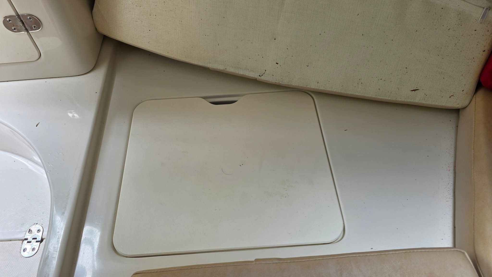 Interior of a boat with a floor hatch and beige upholstery.
