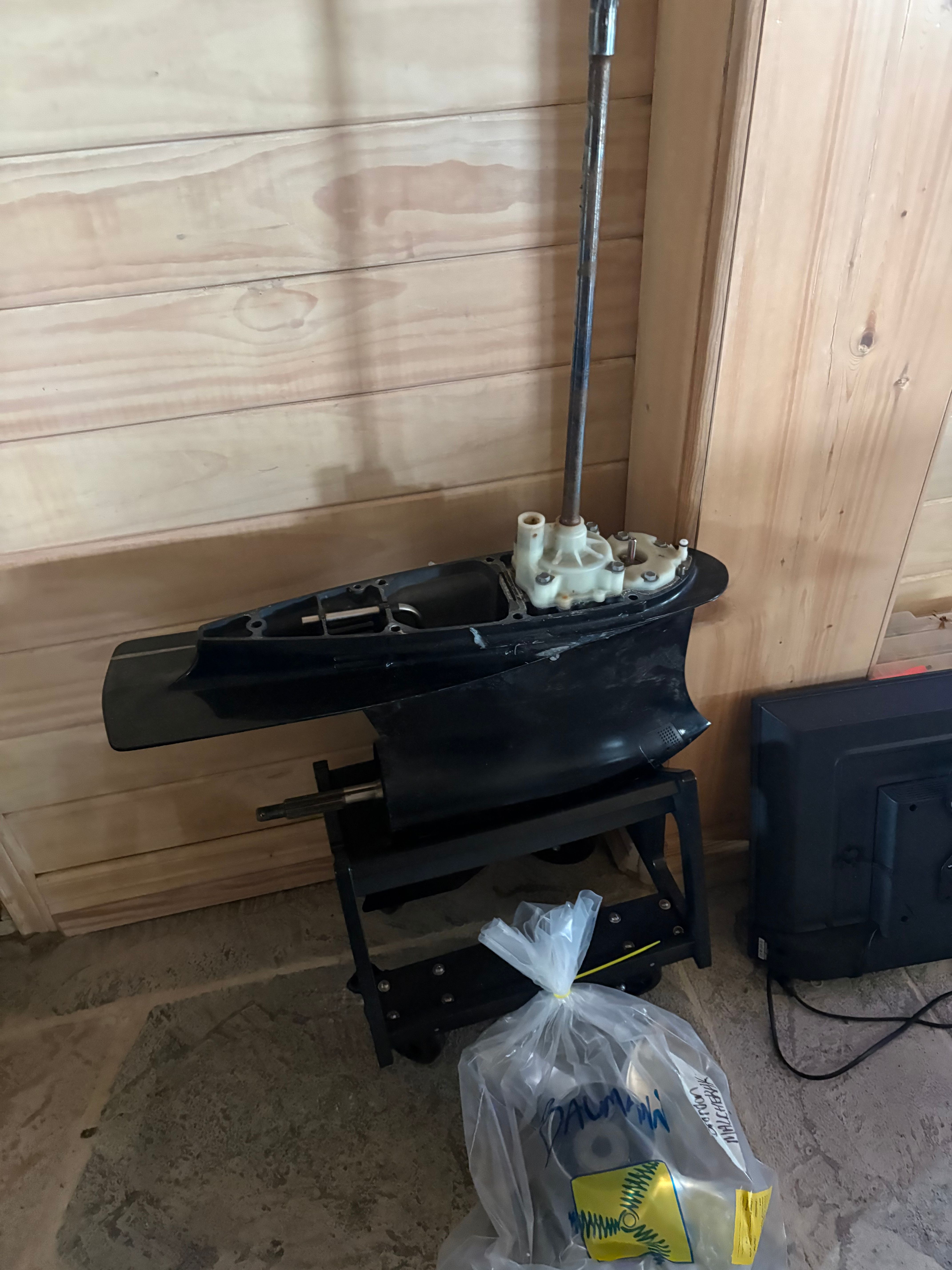 A boat motor is on a stand in front of a wooden wall.