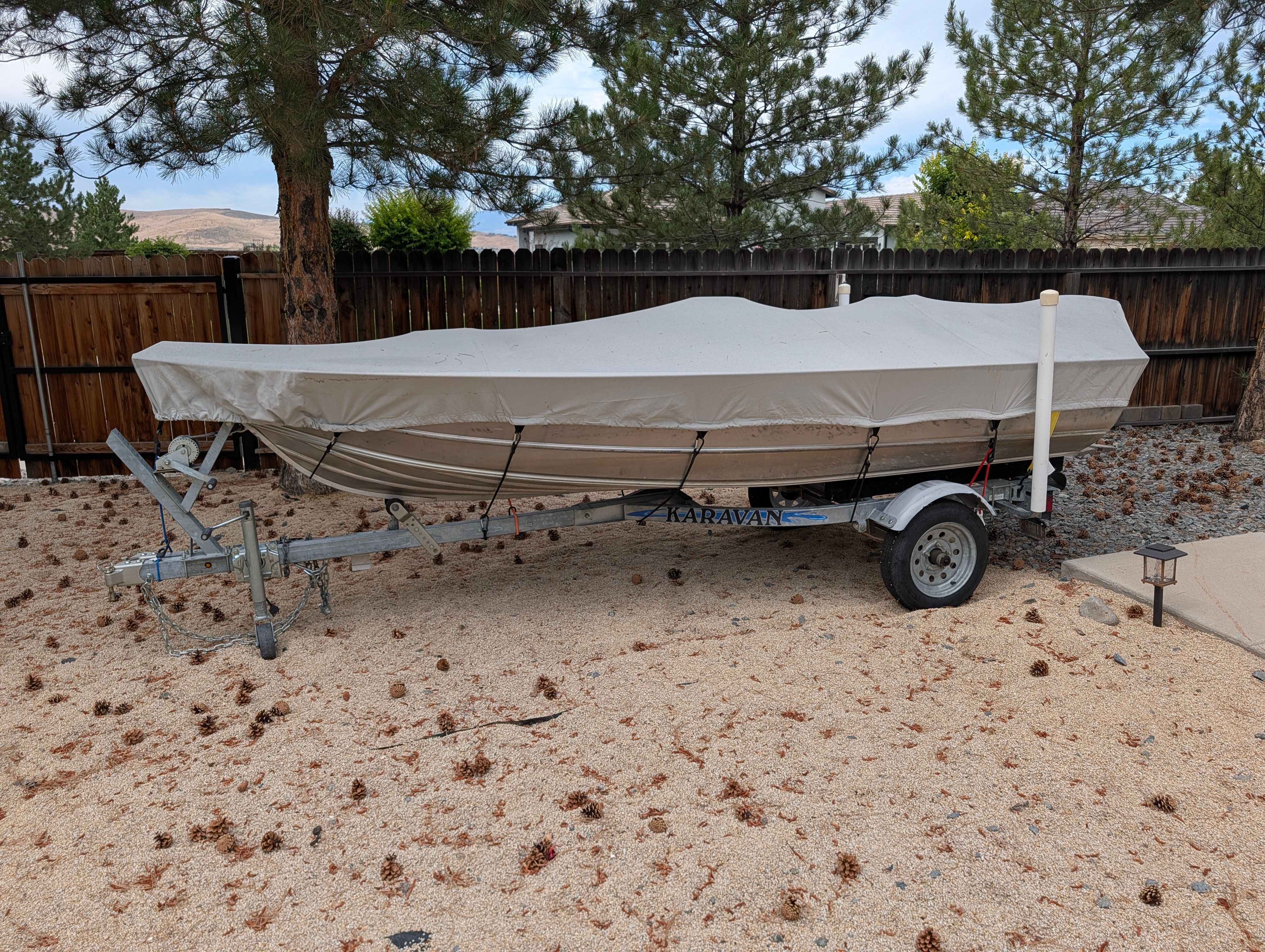 A 2004 Gregor Jon boat on a trailer, covered and parked on a gravel area.