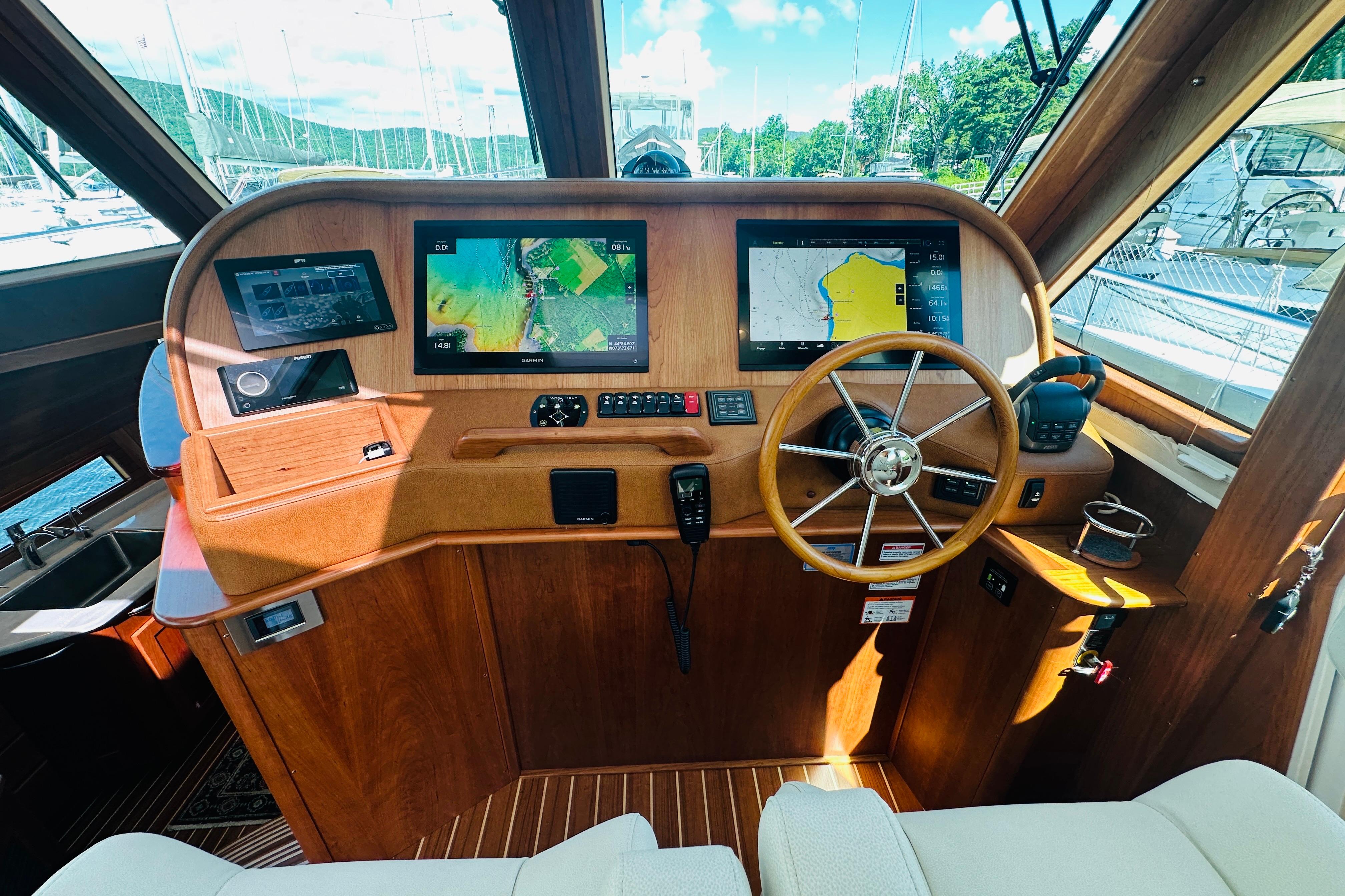 Helm of 2025 Sabre 48 Salon Express with navigation screens and wooden steering wheel.