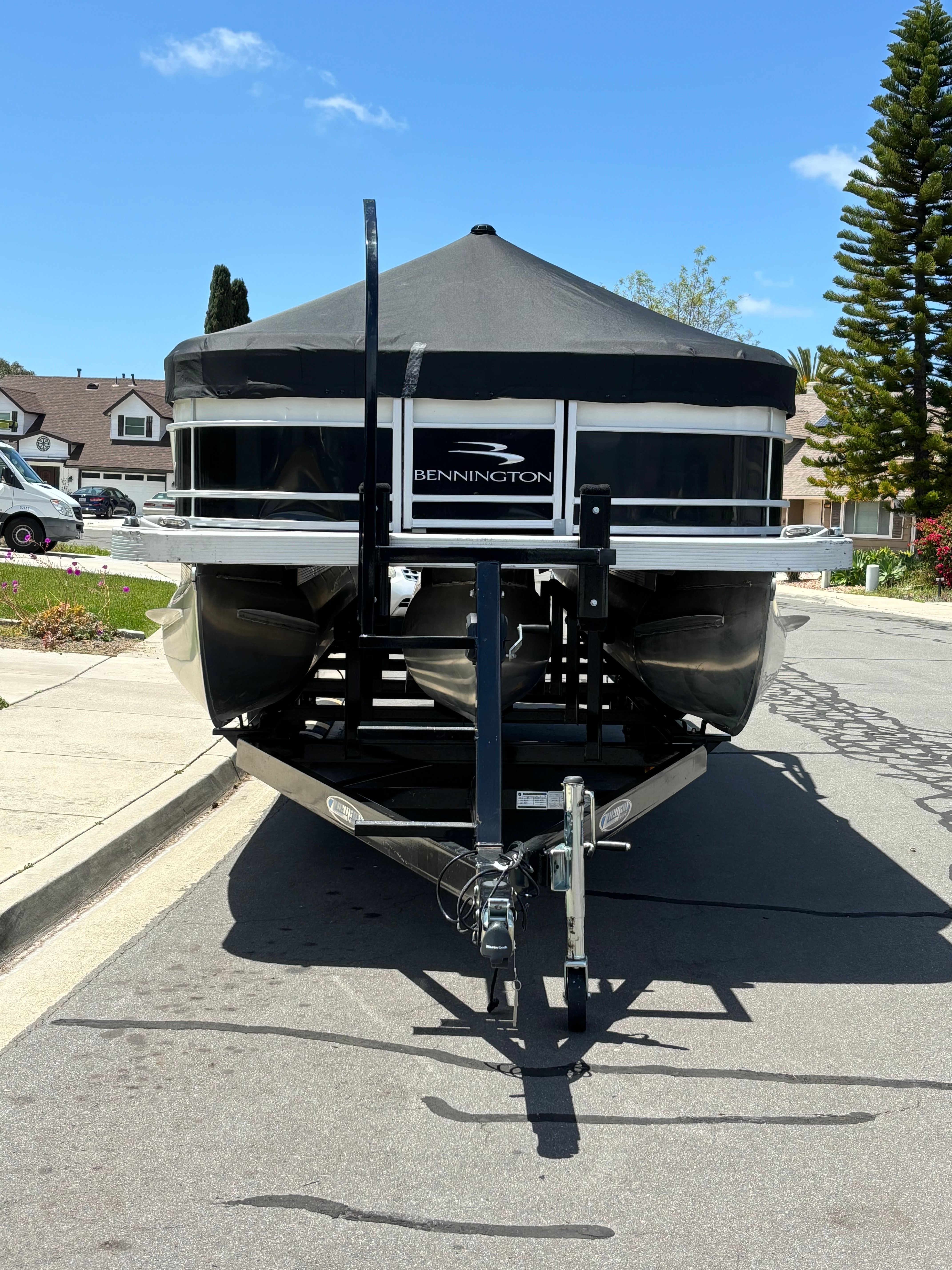 A Bennington L 23 Swingback pontoon boat on a trailer in a residential area.