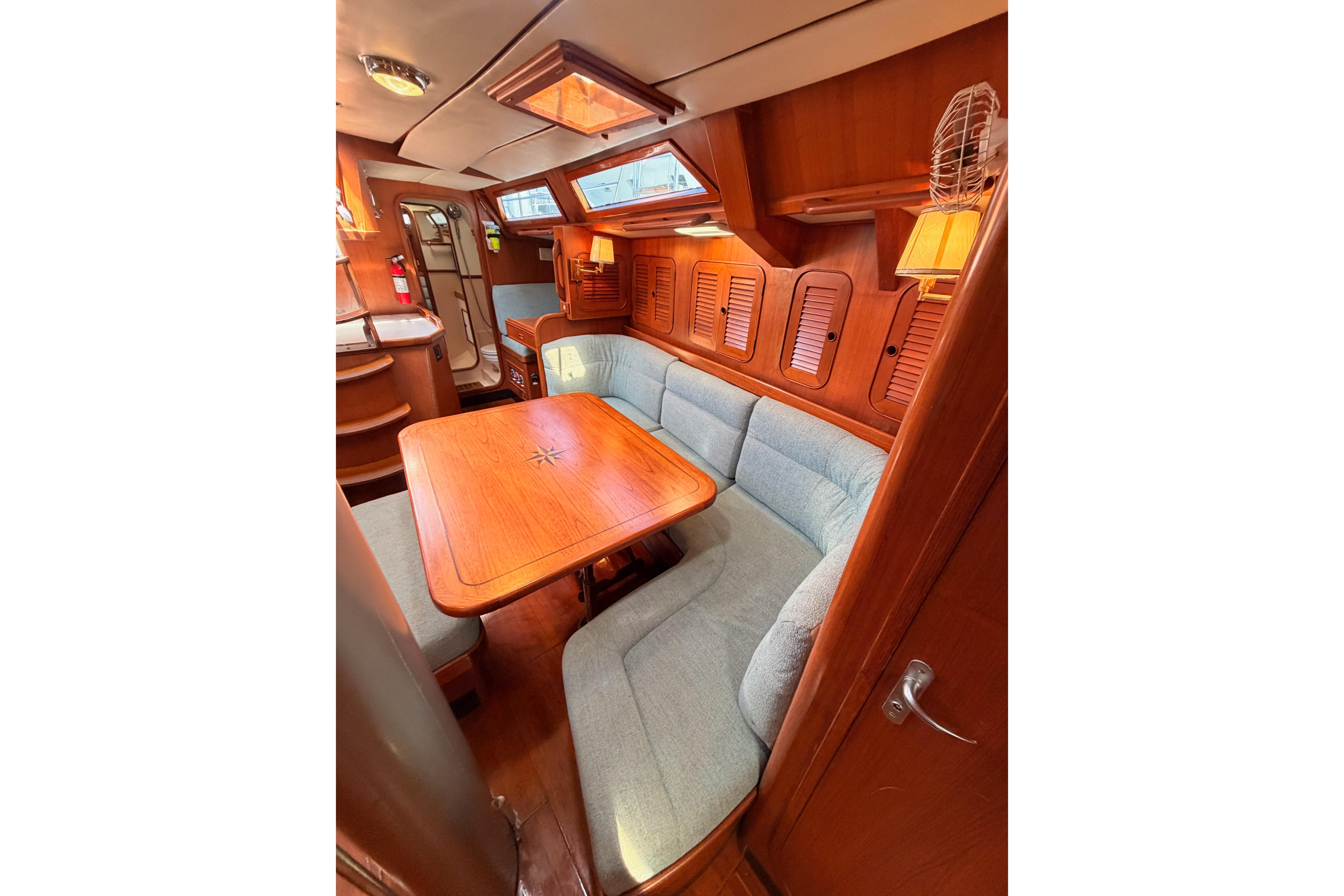 Cozy interior of 1991 Hylas 51 yacht with wooden dining area and cushioned seating.