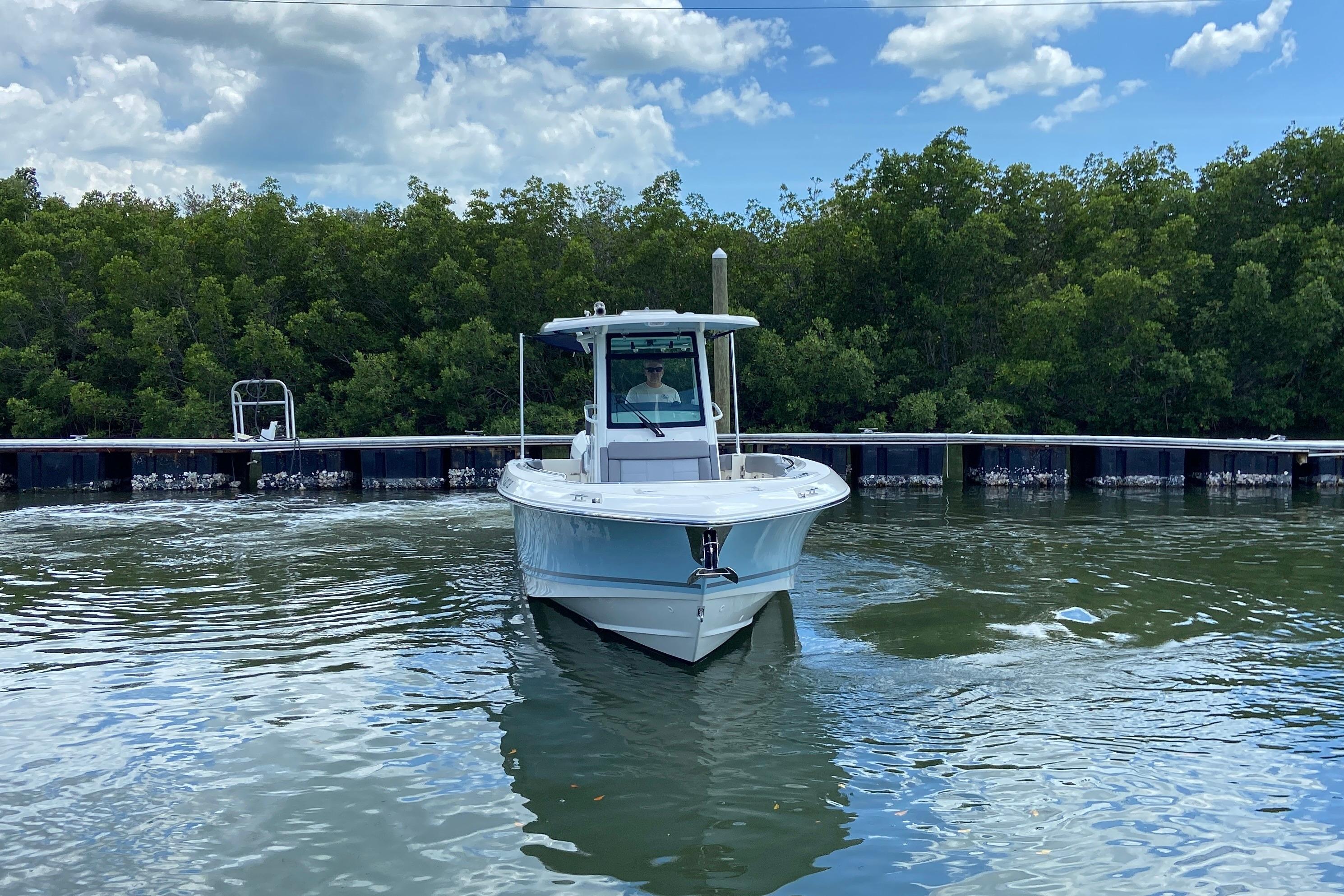 2025 Boston Whaler 280 Outrage boat on calm water near a lush green shoreline.