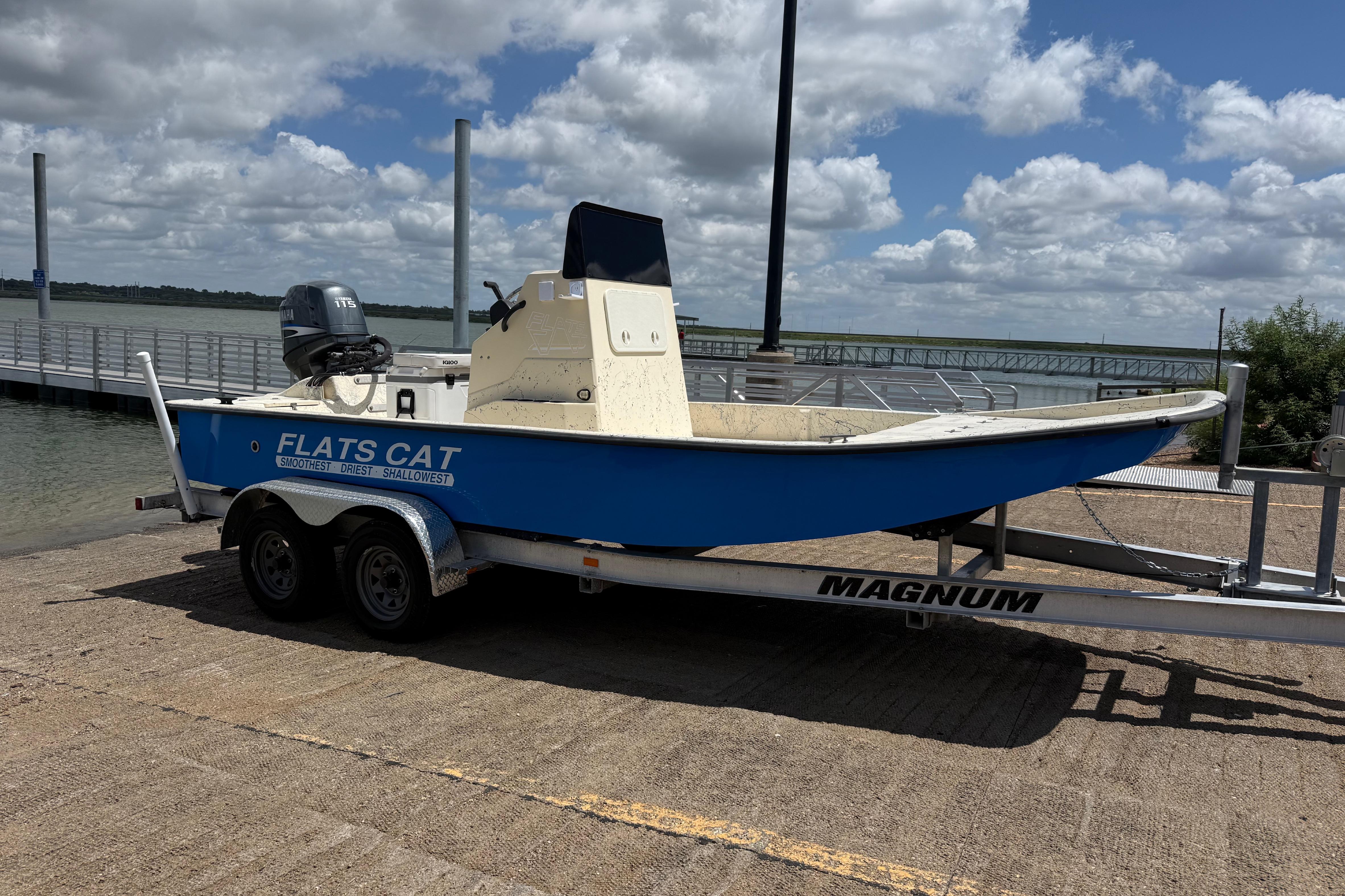 Blue 2007 Flats Cat 19 boat on trailer by waterfront under cloudy sky.