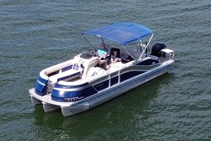 2022 Harris Grand Mariner 250 pontoon boat cruising on a lake with blue canopy.