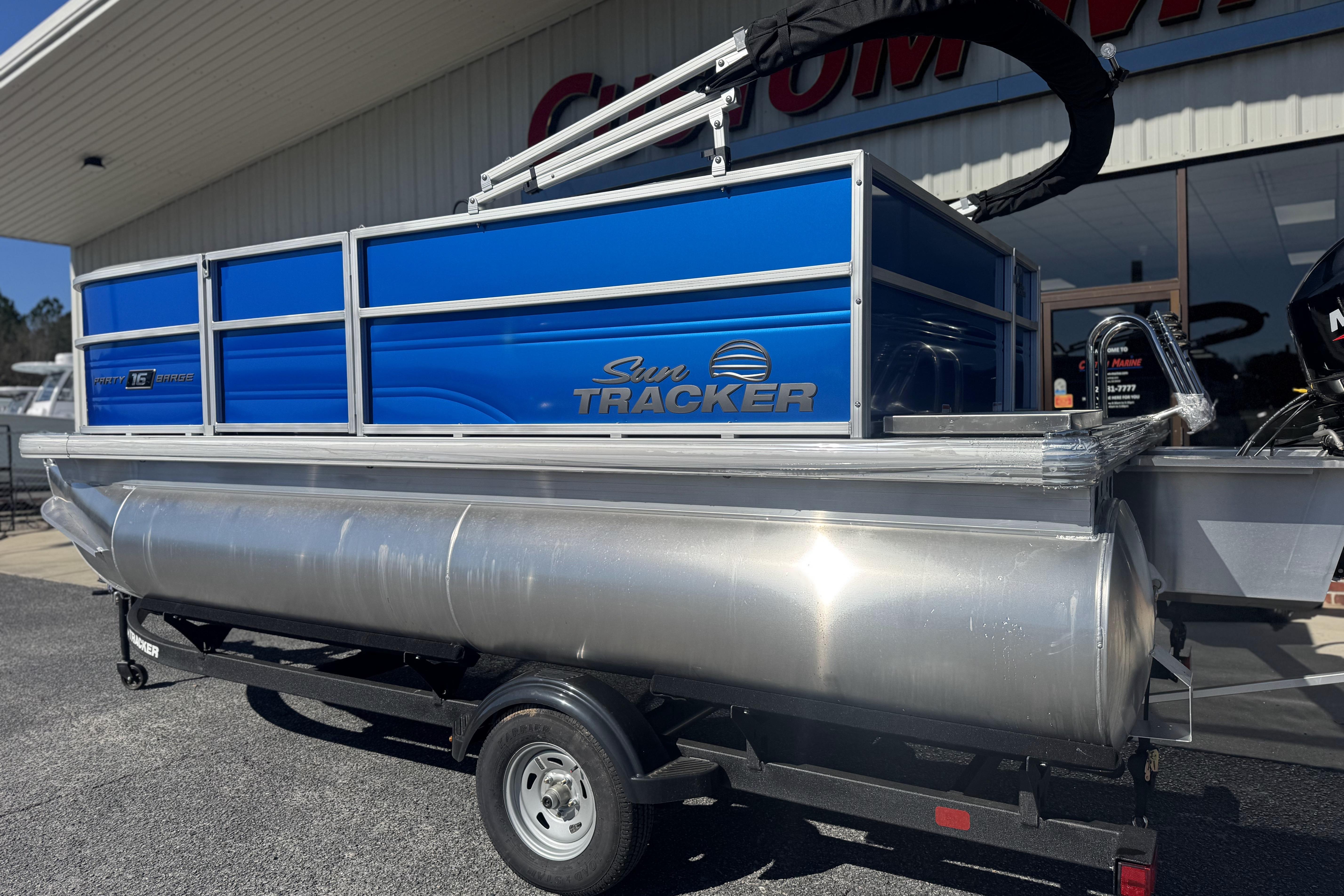 2026 Sun Tracker Party Barge 16 DLX pontoon boat on trailer, blue and silver design.