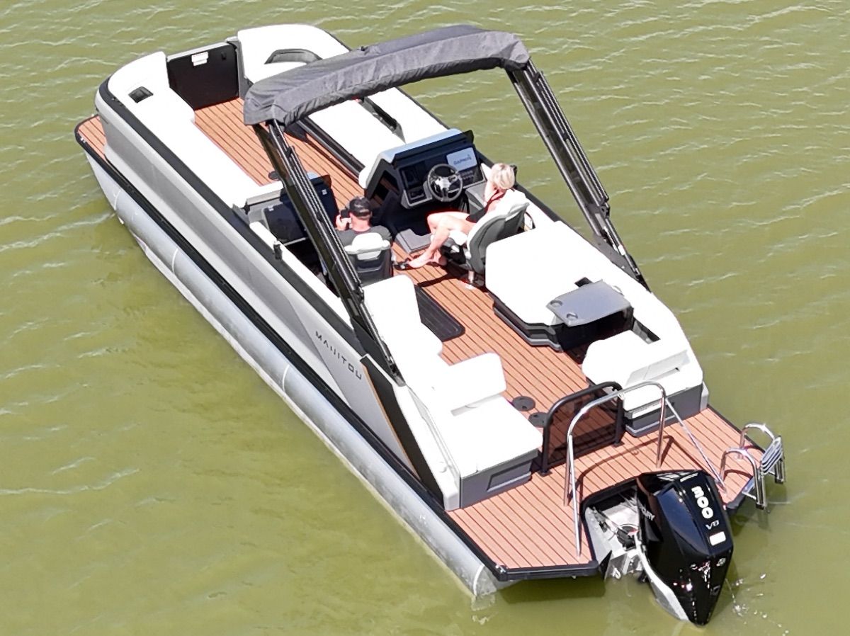 A modern pontoon boat with a wooden deck and sunshade on calm water.