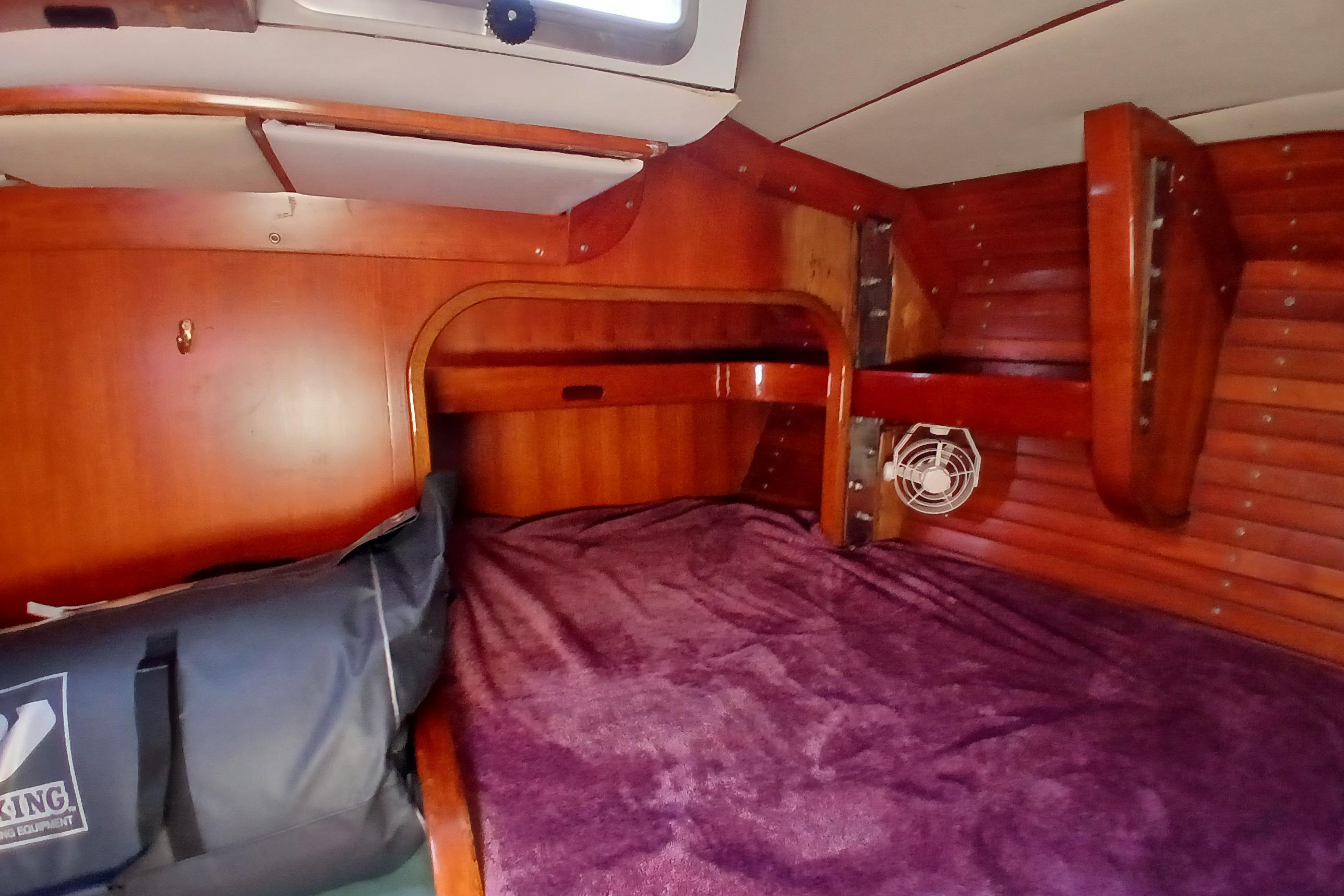 Cozy cabin interior of 1981 SKYE 51 sailboat with wooden finish and purple bedding.