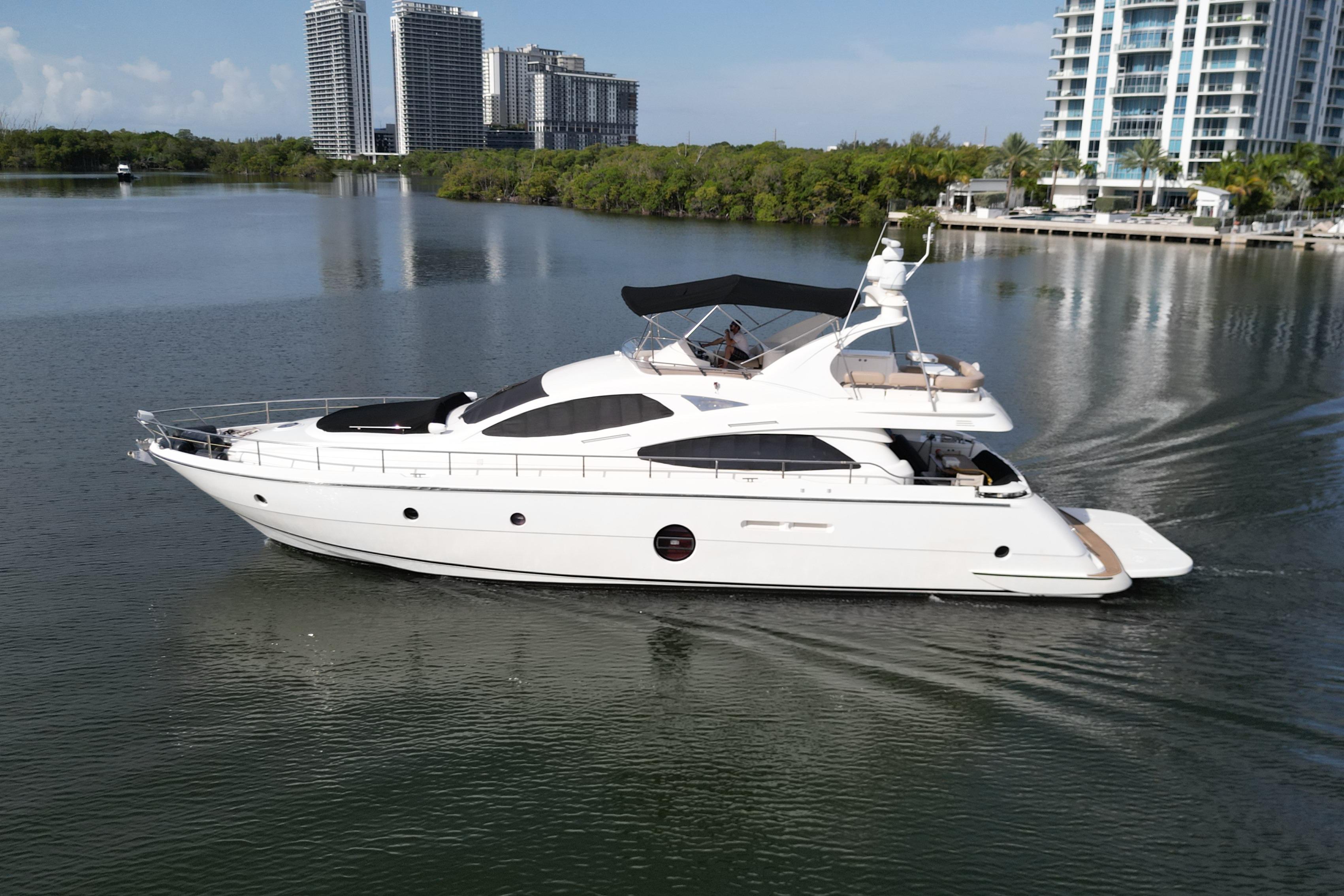 2006 Aicon Flybridge yacht cruising on calm waters near modern high-rise buildings.