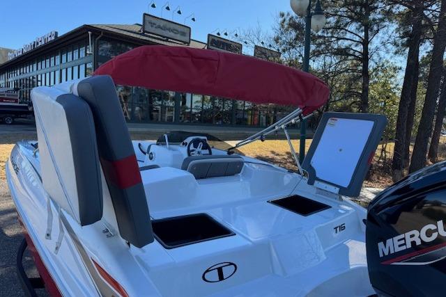 2026 Tahoe T16 boat with red canopy and Mercury engine, parked near a building.