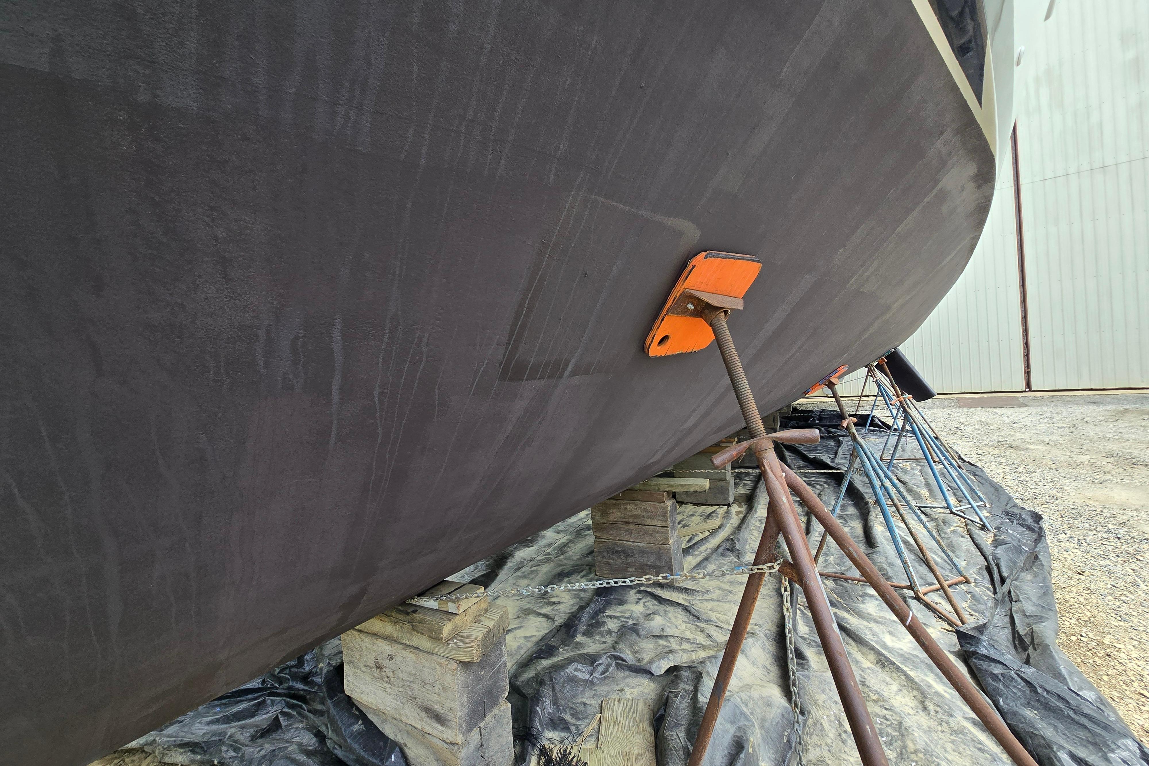 1980 Hatteras 70 Motor Yacht hull supported on stands in a boatyard.