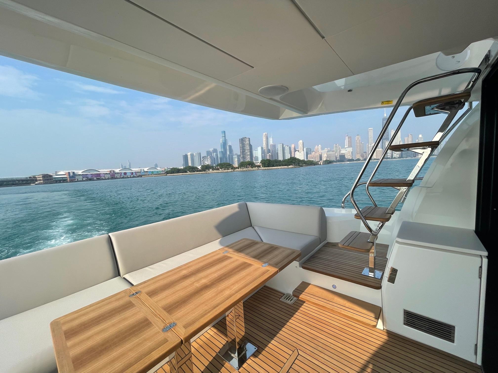 Luxurious 2024 Prestige 520 Flybridge yacht with city skyline view, featuring elegant deck seating.