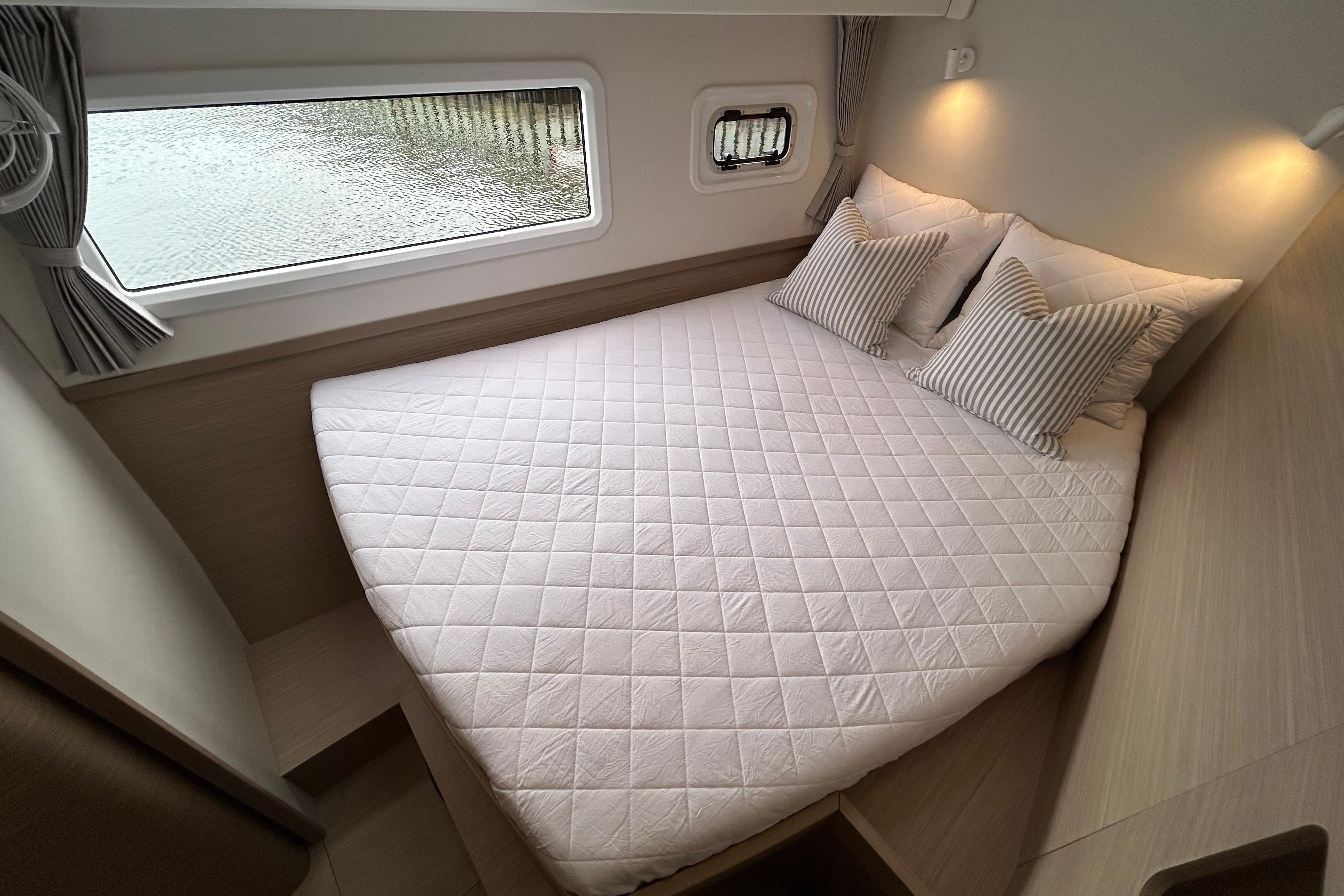 Luxurious cabin interior of 2024 Lagoon 42 catamaran with cozy bed and window view.