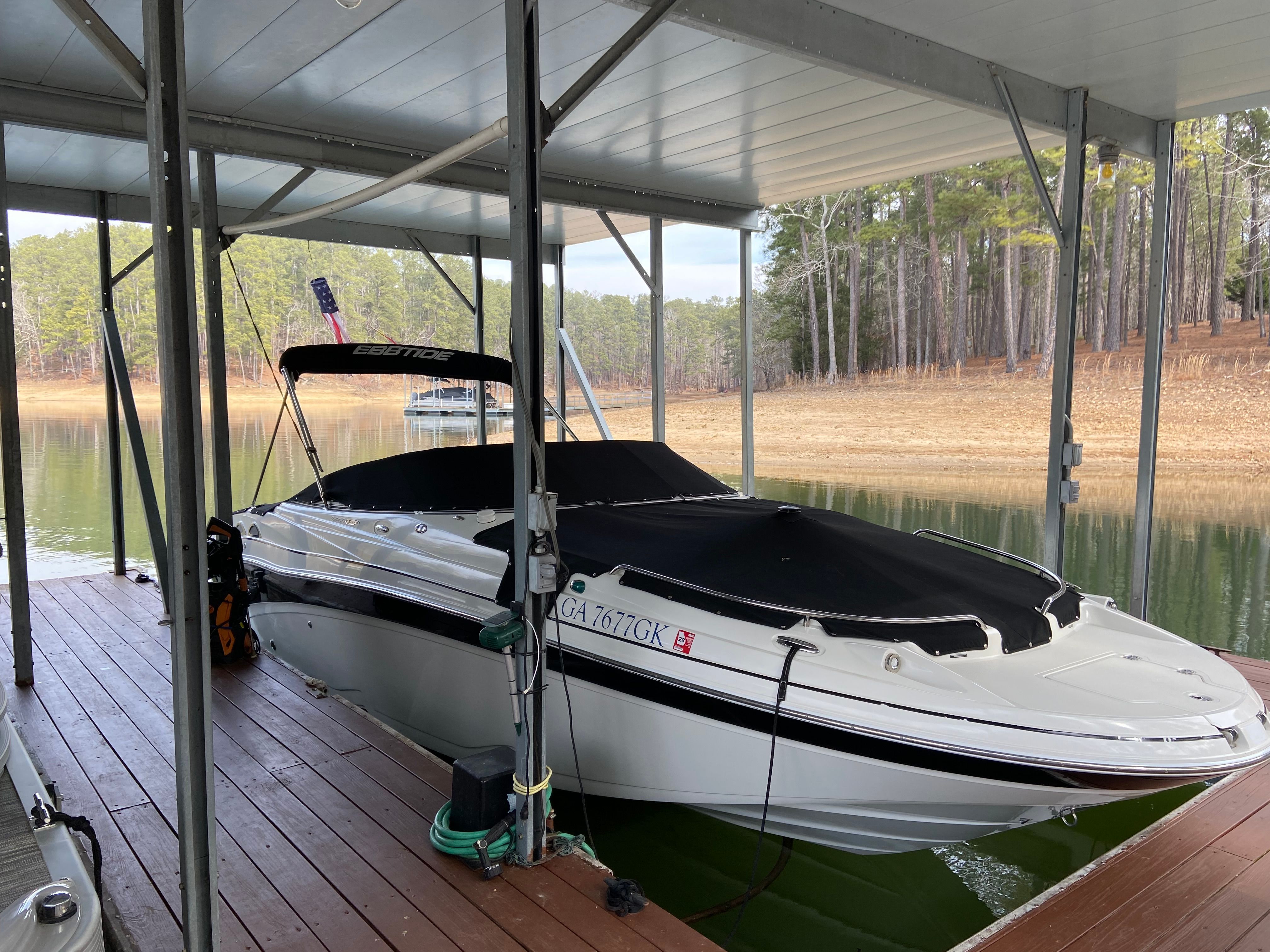 A white 2007 Ebbtide 2460 Z-Trak boat is docked under a covered area on a calm lake.