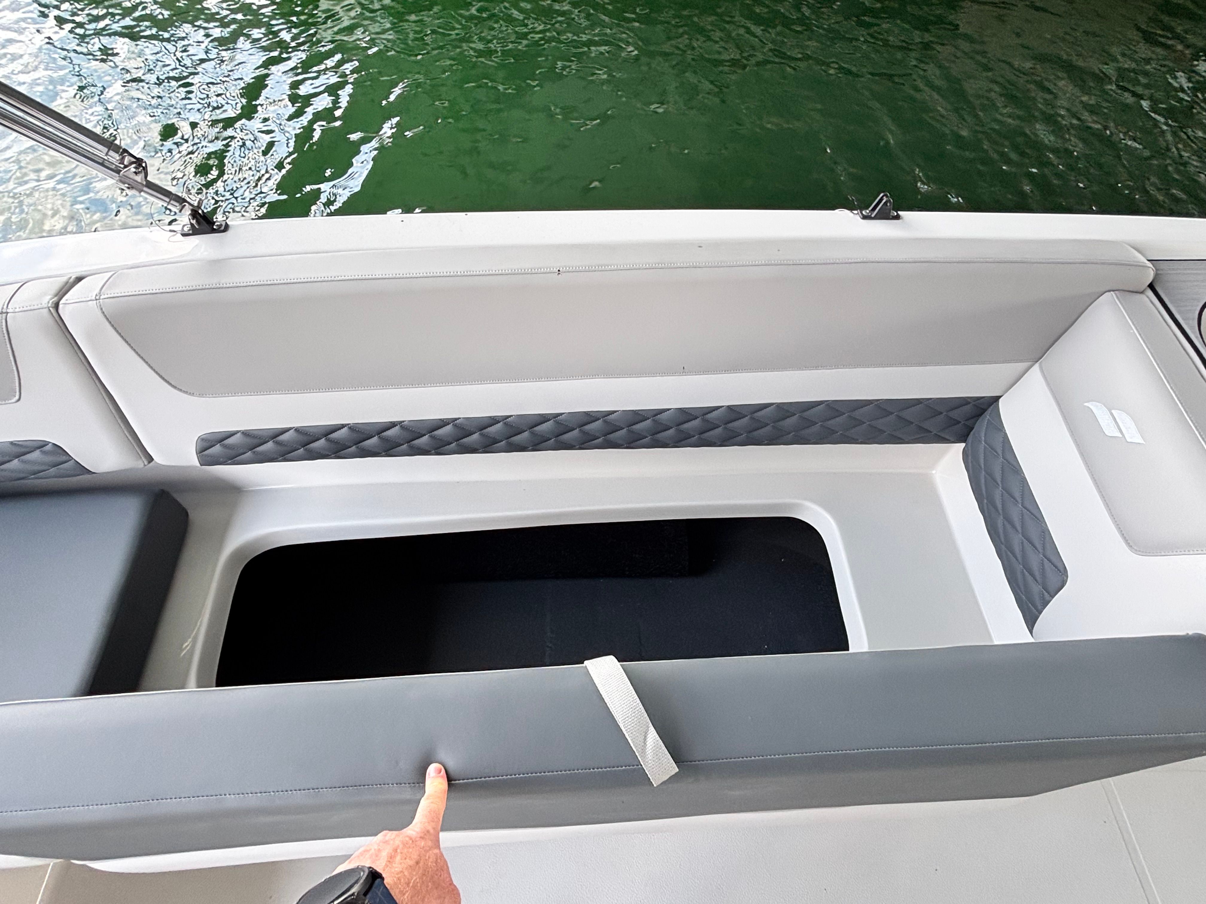 A gray boat with cushioned seating and storage underneath, floating on green water.