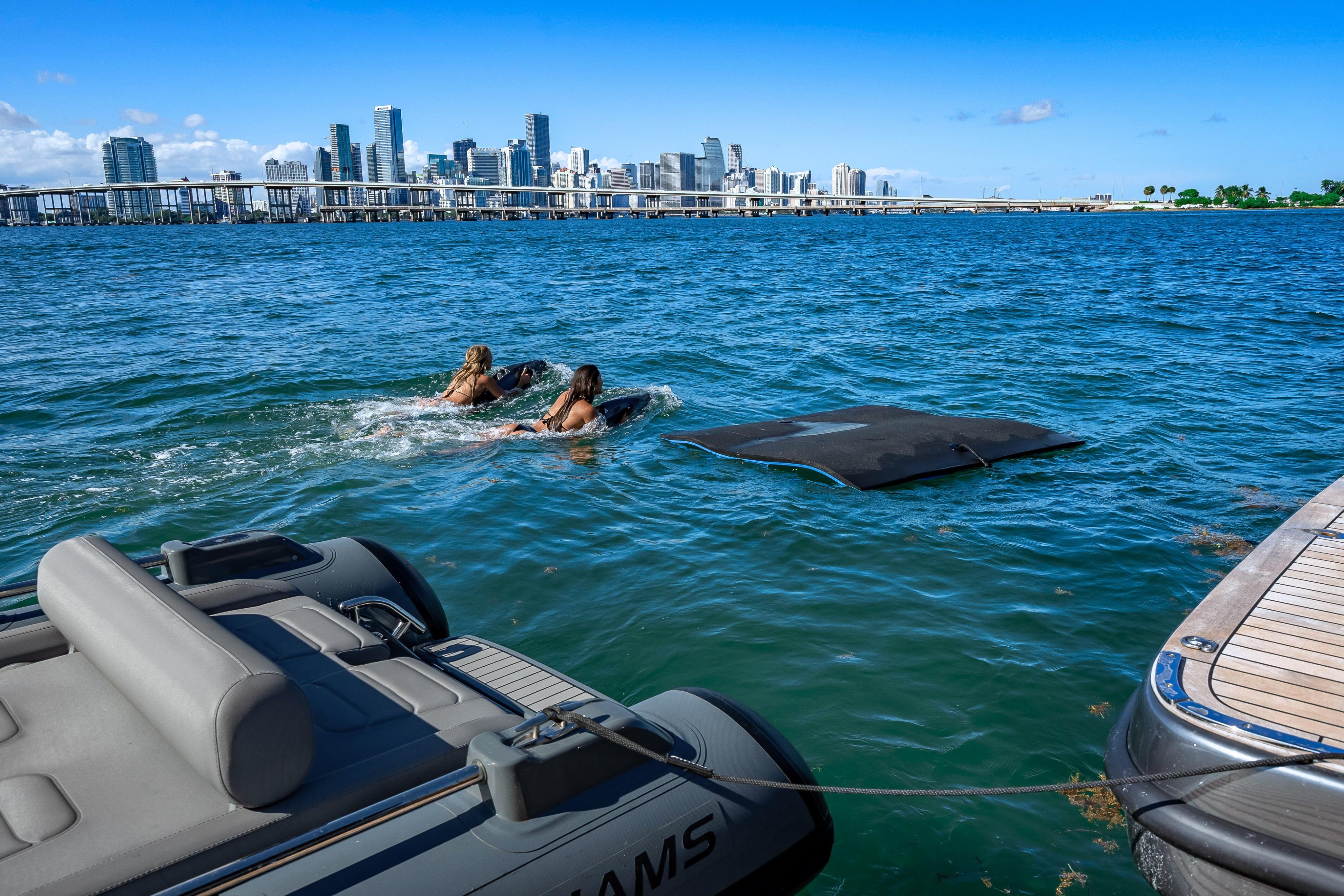 Two people swimming near a Sunreef 60 Power yacht, city skyline in background.