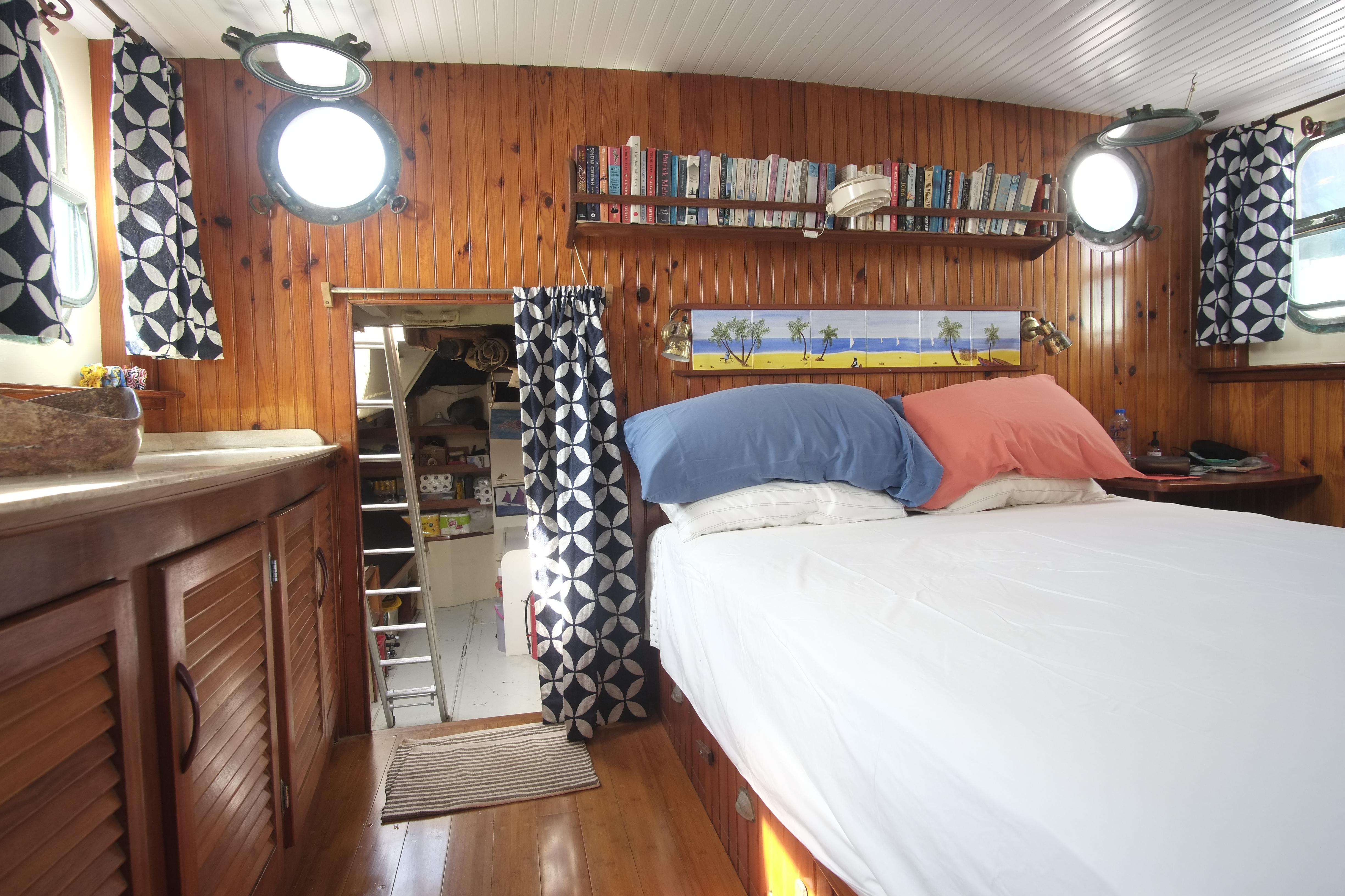 Cozy 1930 Custom Gronigen boat cabin with wood paneling, bed, bookshelves, and nautical decor.