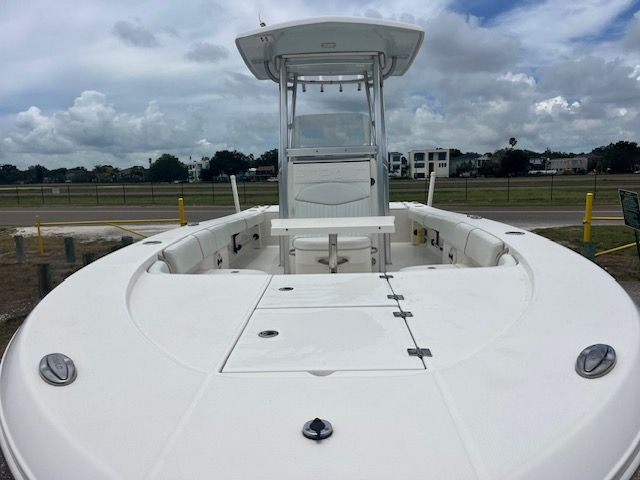 A white boat with an open deck and T-top, parked on a lot with cloudy skies.