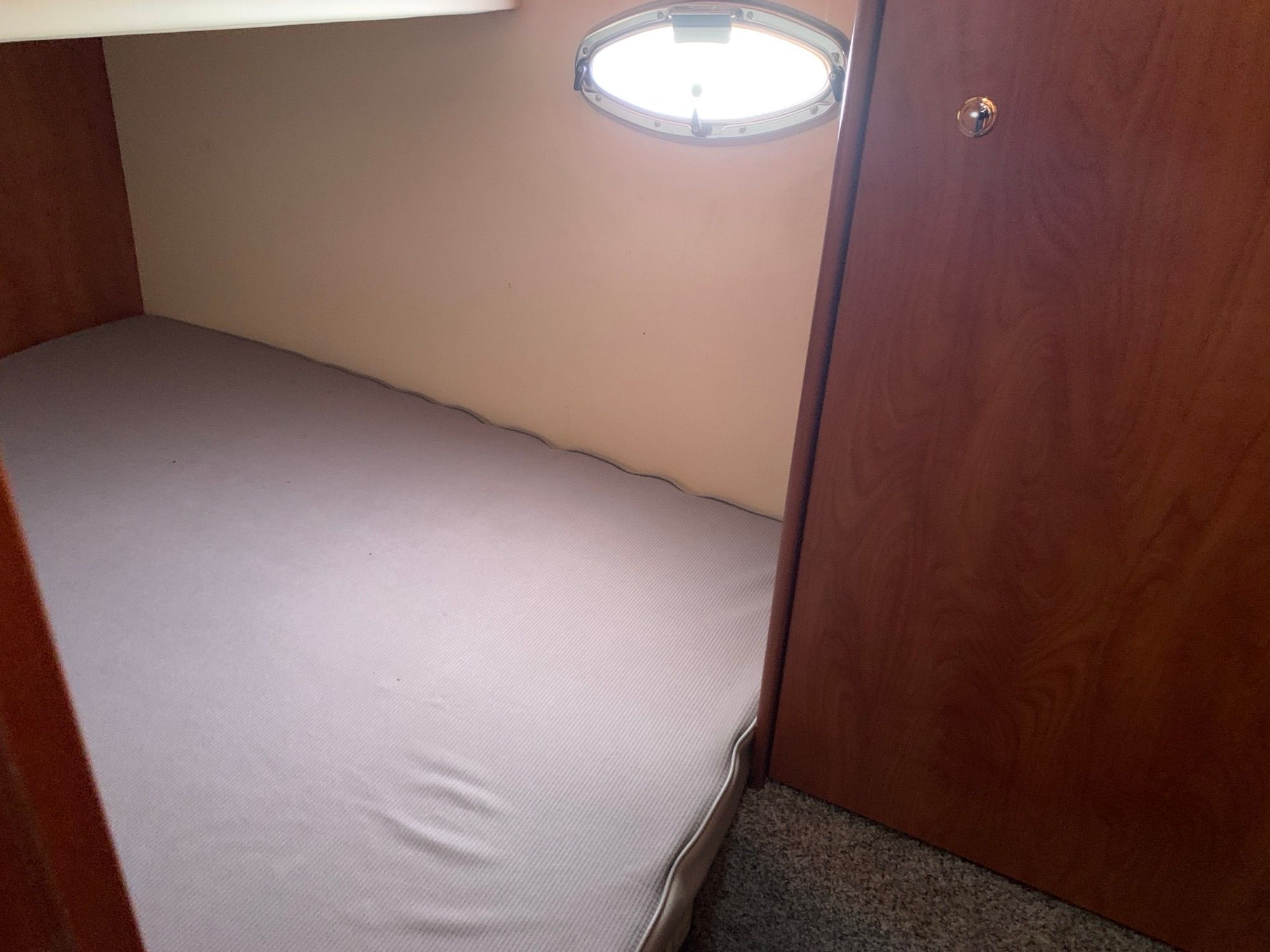 Small cabin with a bed and a porthole on the wall.