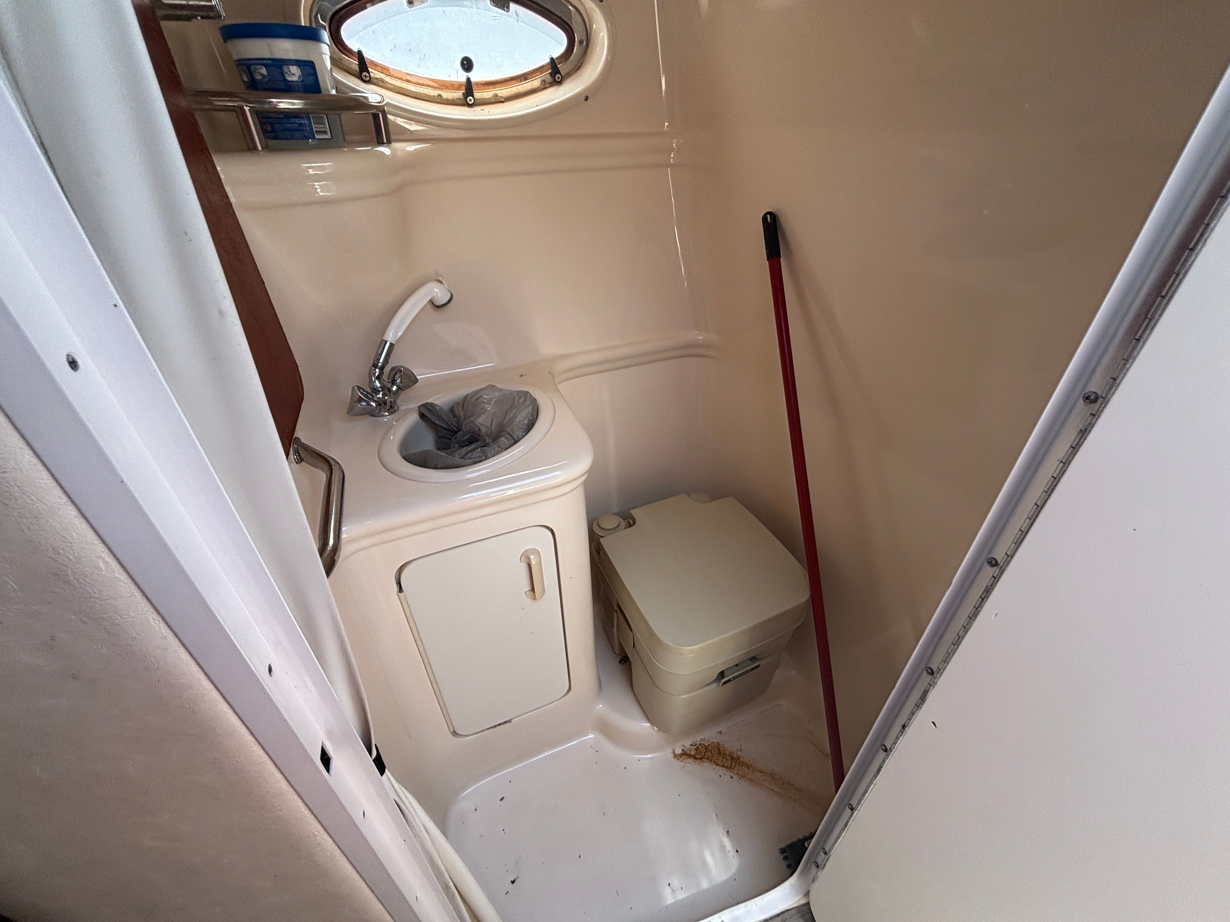 Small bathroom with sink, toilet, and porthole on a boat.