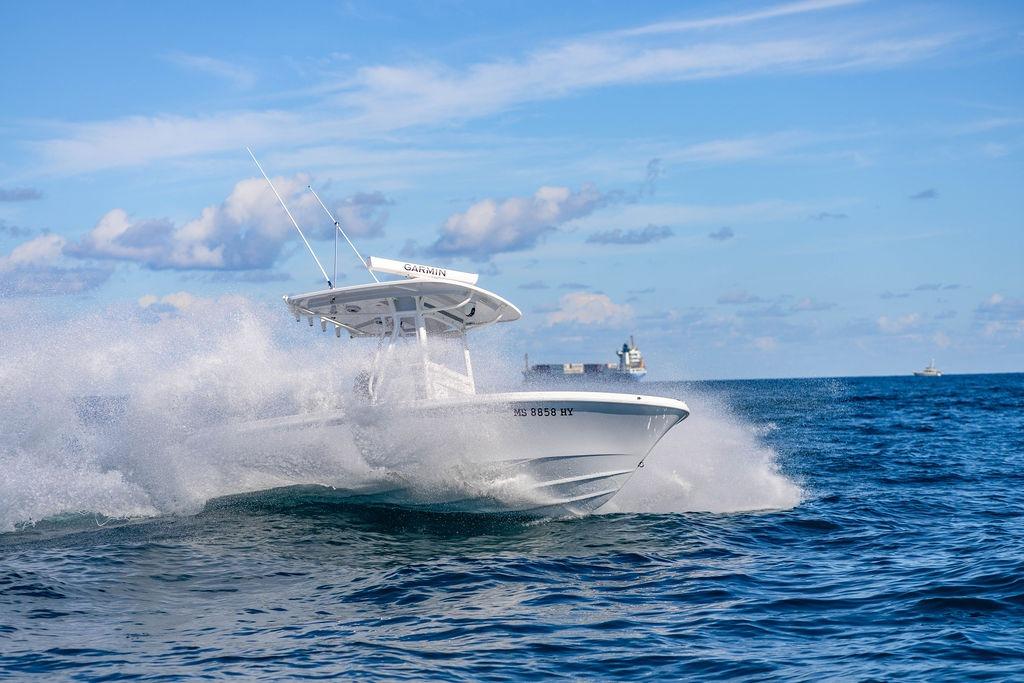 2024 Reef Runner 230 Open boat cruising on ocean waves under a clear blue sky.