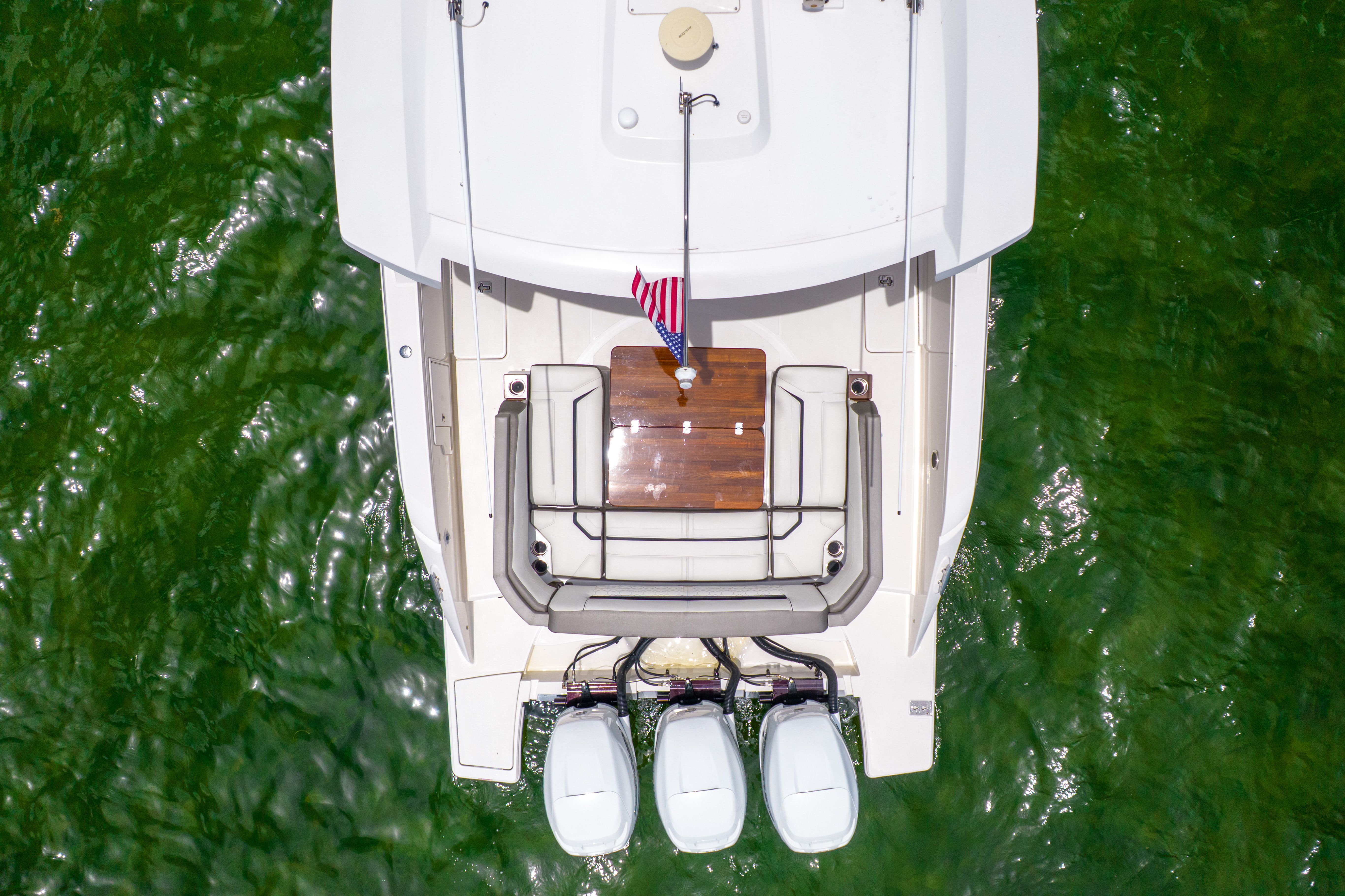 Aerial view of a 2023 Tiara Yachts 38 LS on green water, featuring three outboard engines.