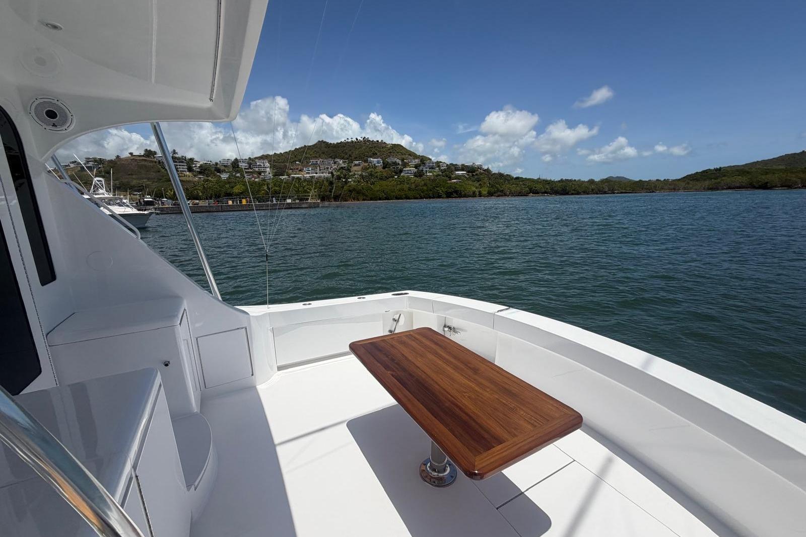 2003 Hatteras 54 Convertible yacht deck with wooden table, overlooking scenic coastal view.