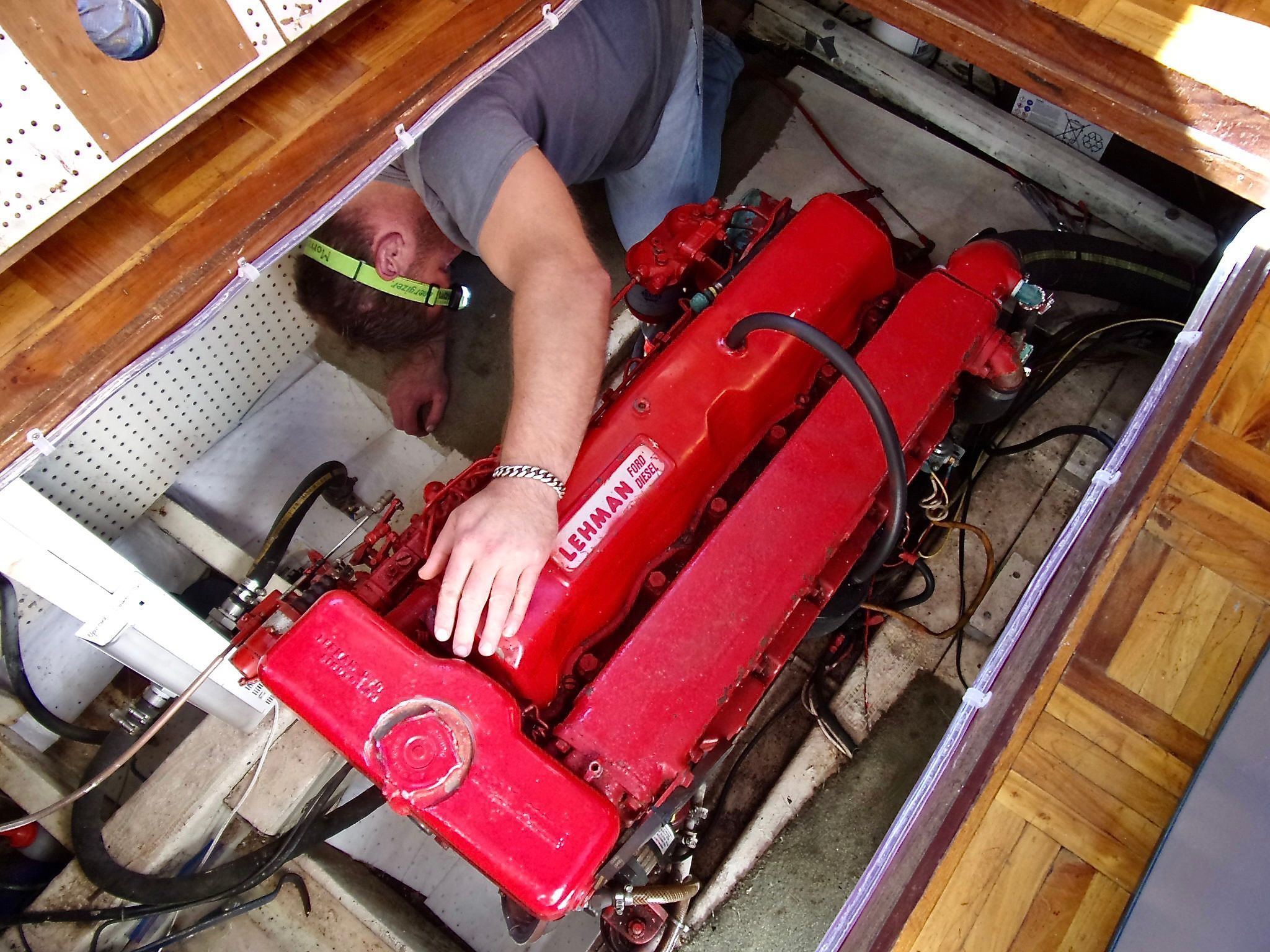 Mechanic working on red Lehman diesel engine in 1976 CHB Trawler boat.