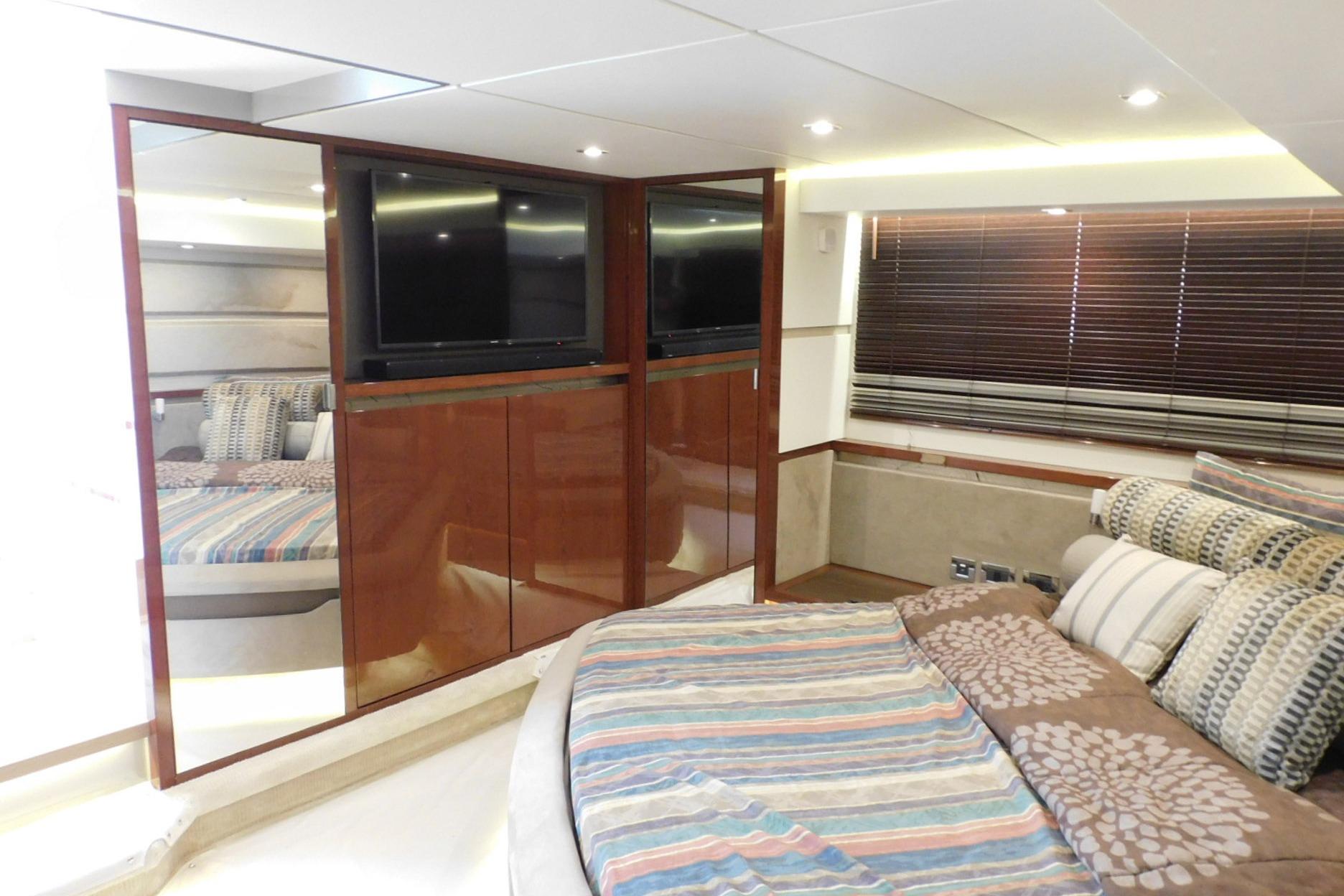Luxurious 2019 Sea Ray L550 yacht bedroom with striped bedding and wooden cabinetry.