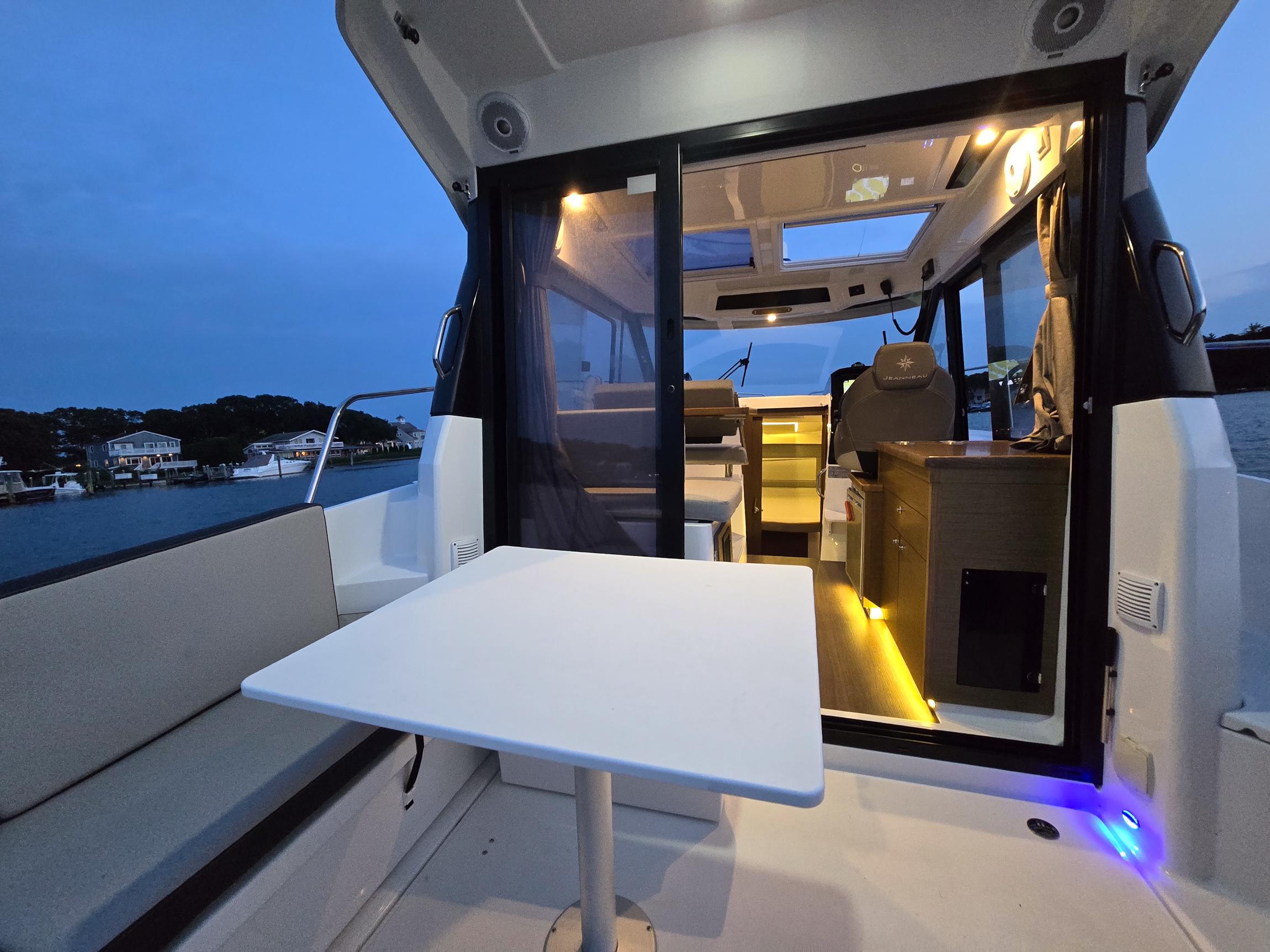 2021 Jeanneau NC895 boat interior with seating and table, illuminated at dusk.