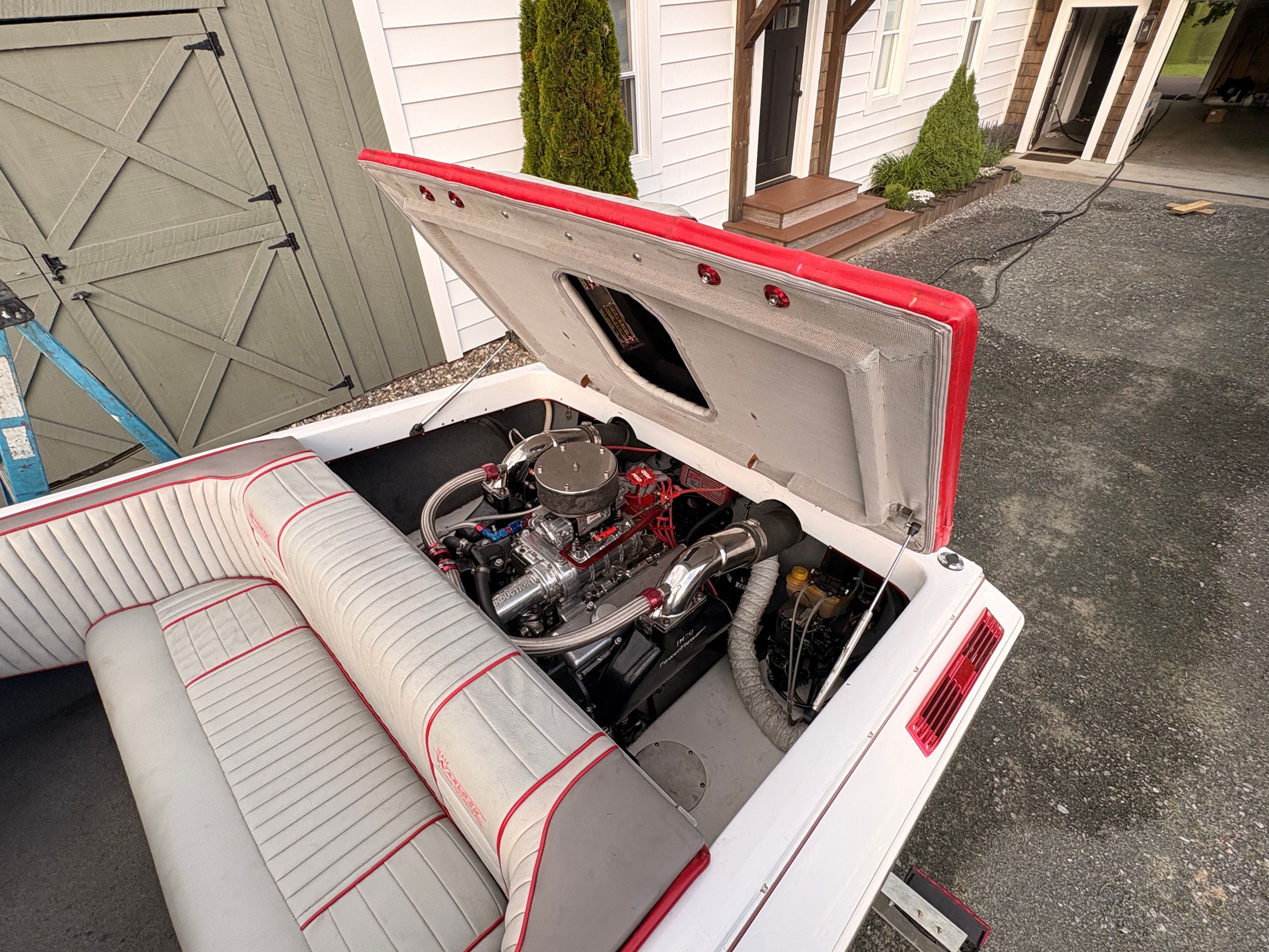 A 1986 Warlock 23 boat with an open engine compartment. The interior features white upholstery with red accents.