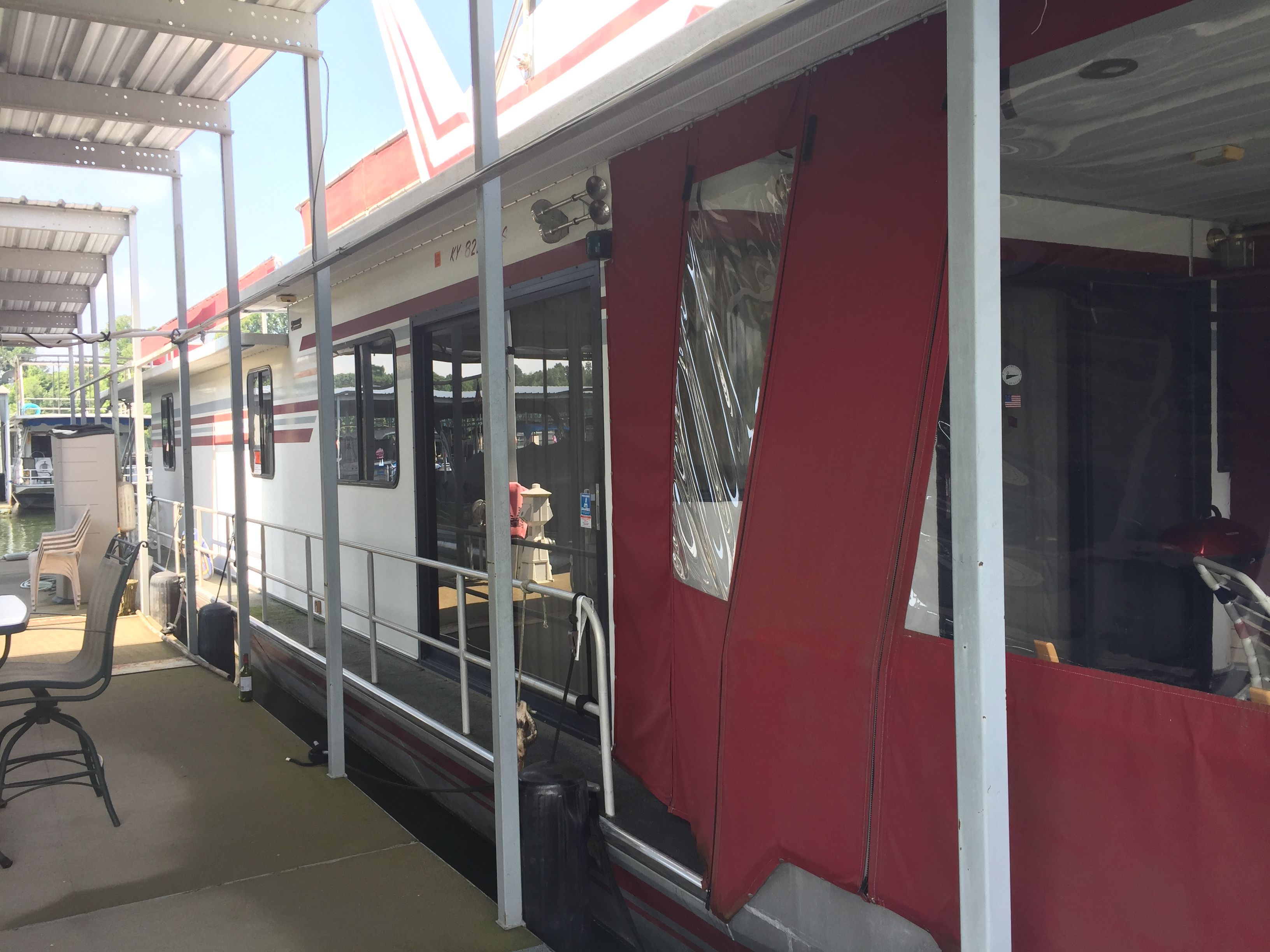 A 1989 Sumerset houseboat with red canopy, docked at a marina.