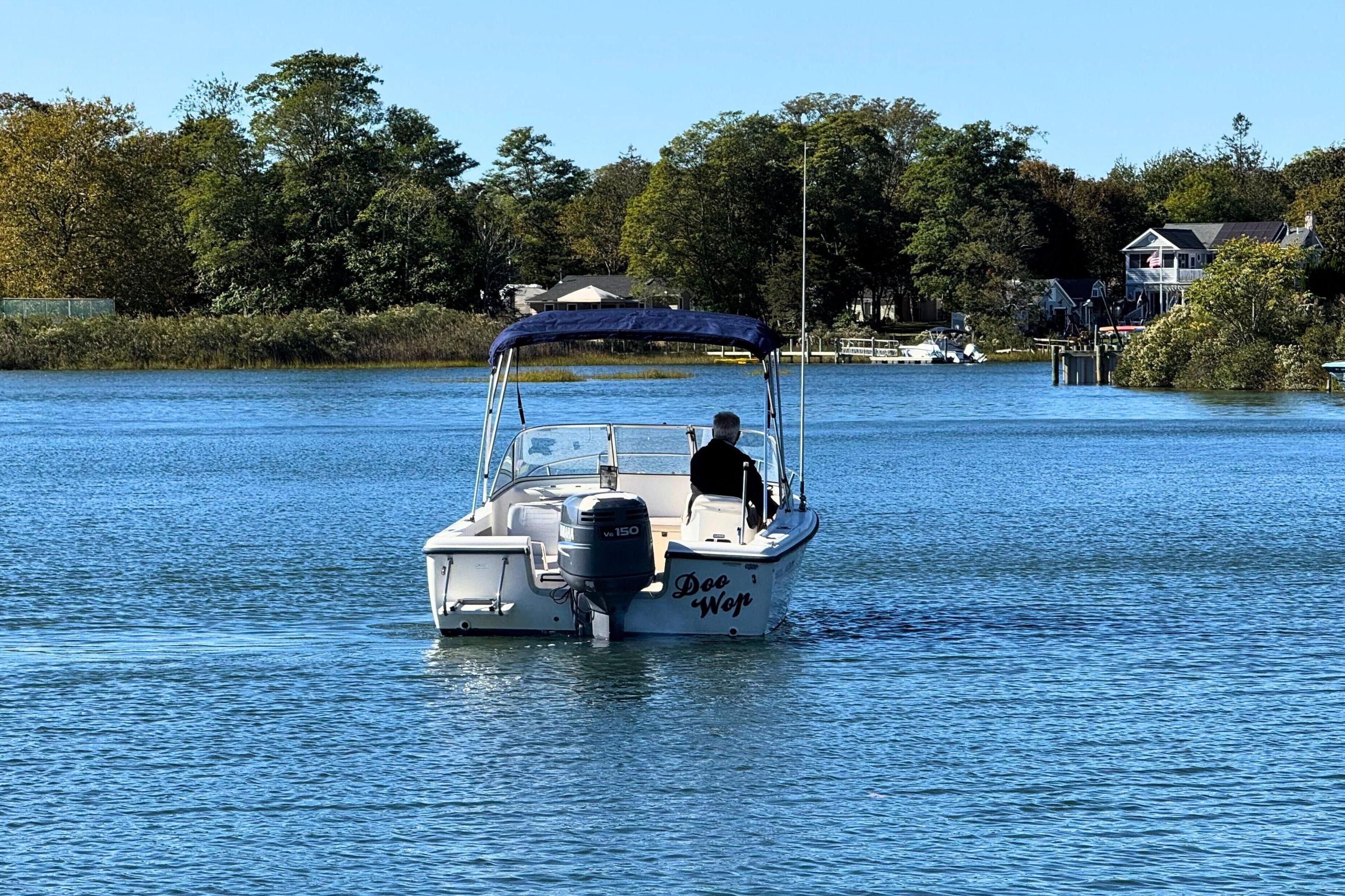 A 2002 Sea Hunt Escape 200 boat cruising on a serene lake with lush greenery.