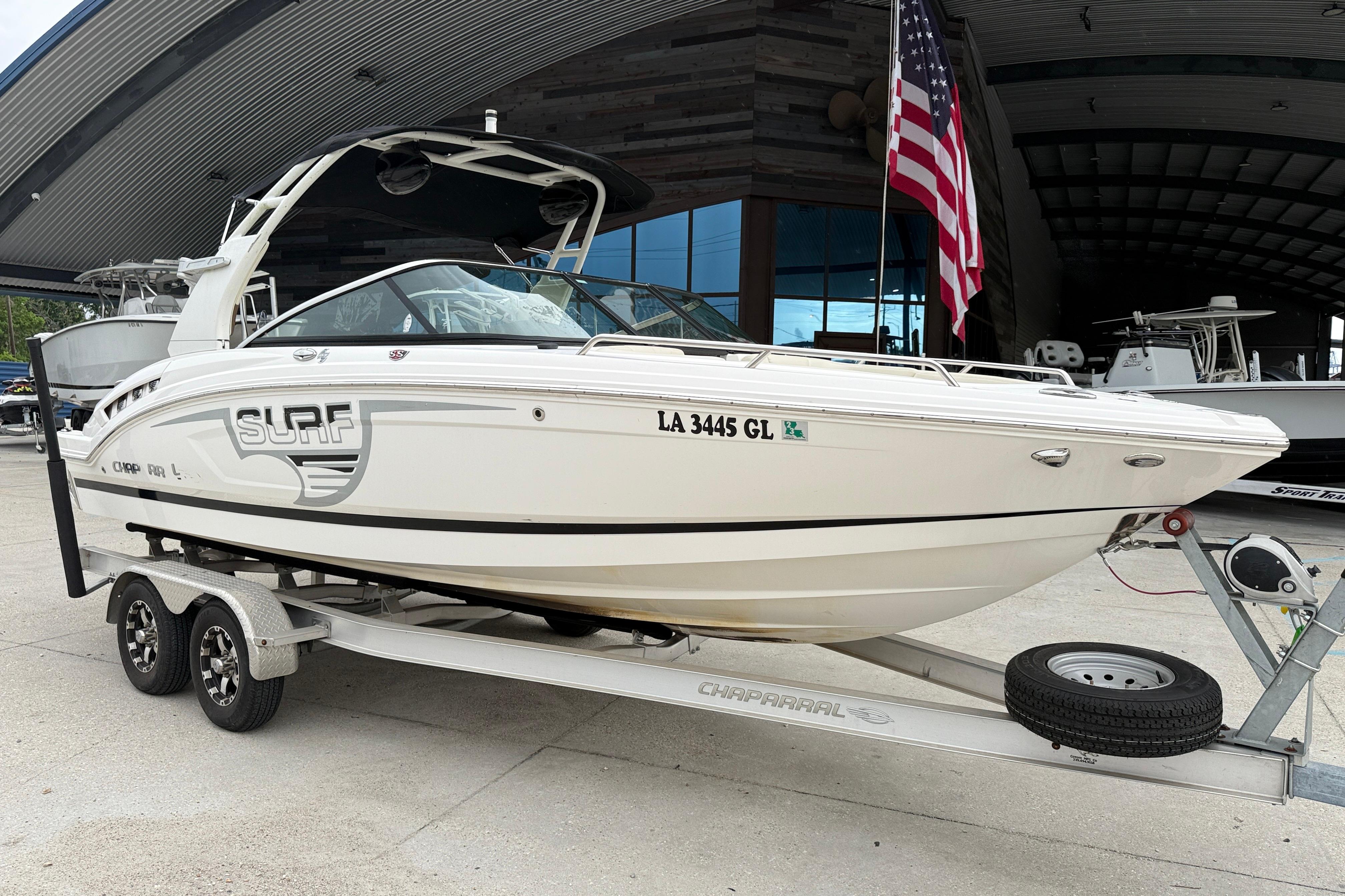 2018 Chaparral 227 SSX Surf boat on trailer, parked near a building with an American flag.