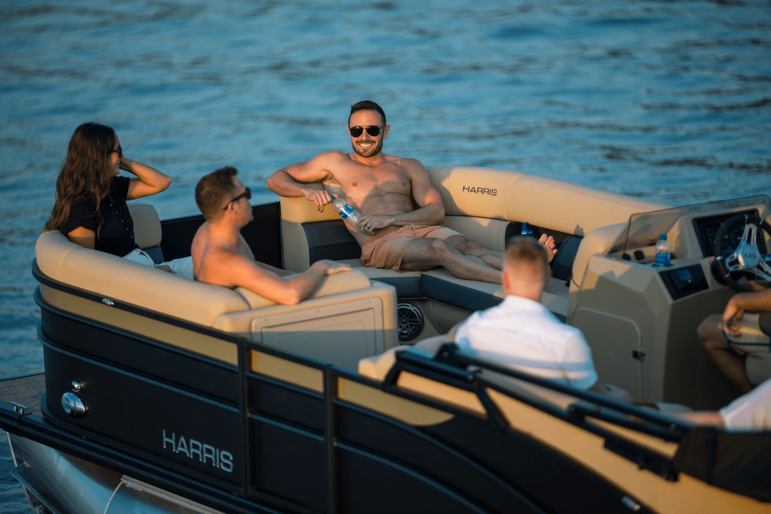 Four people relax on a Harris Cruiser 230 pontoon boat on the water.