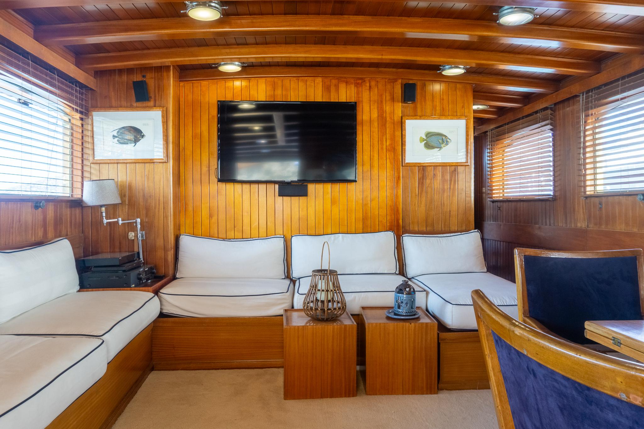 Luxurious wooden yacht interior with white seating, TV, and nautical decor, Psarros Shipyard 1969.