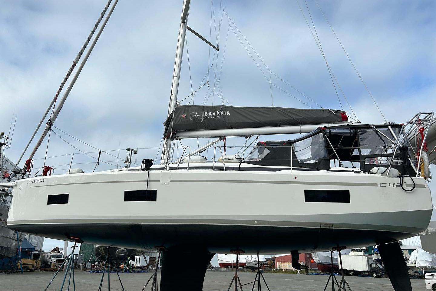 2021 Bavaria C42 sailboat on stands, displayed in a shipyard under a cloudy sky.
