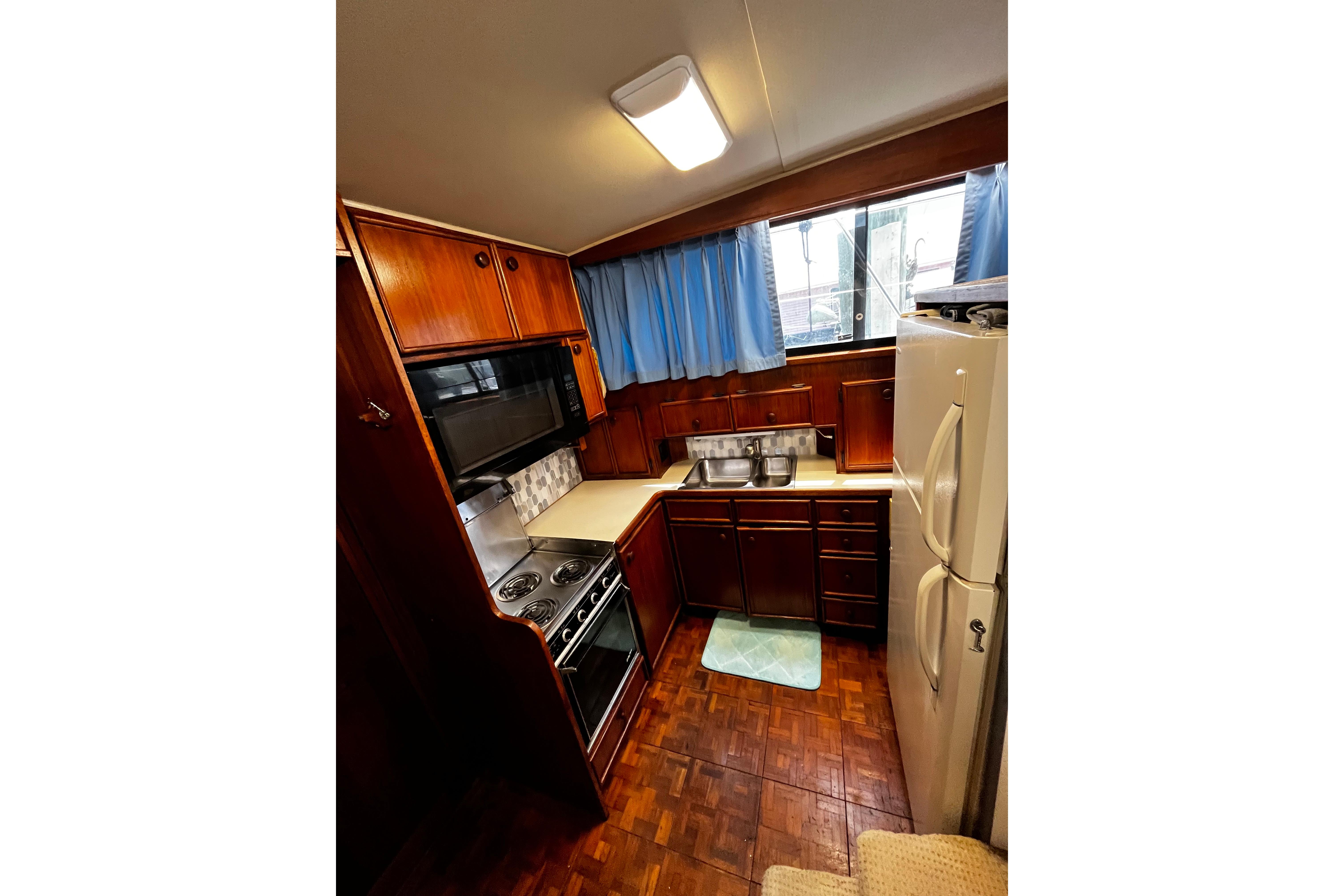 1988 Chris Craft Constellation kitchen with wood cabinetry, stove, microwave, and refrigerator.